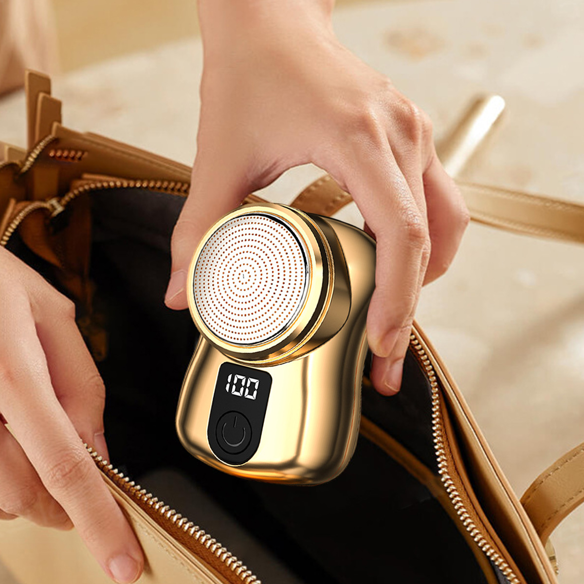 Eine Hand hält einen goldenen, kompakten Rasierer mit digitaler Anzeige und Netzteil über einer offenen Tasche.