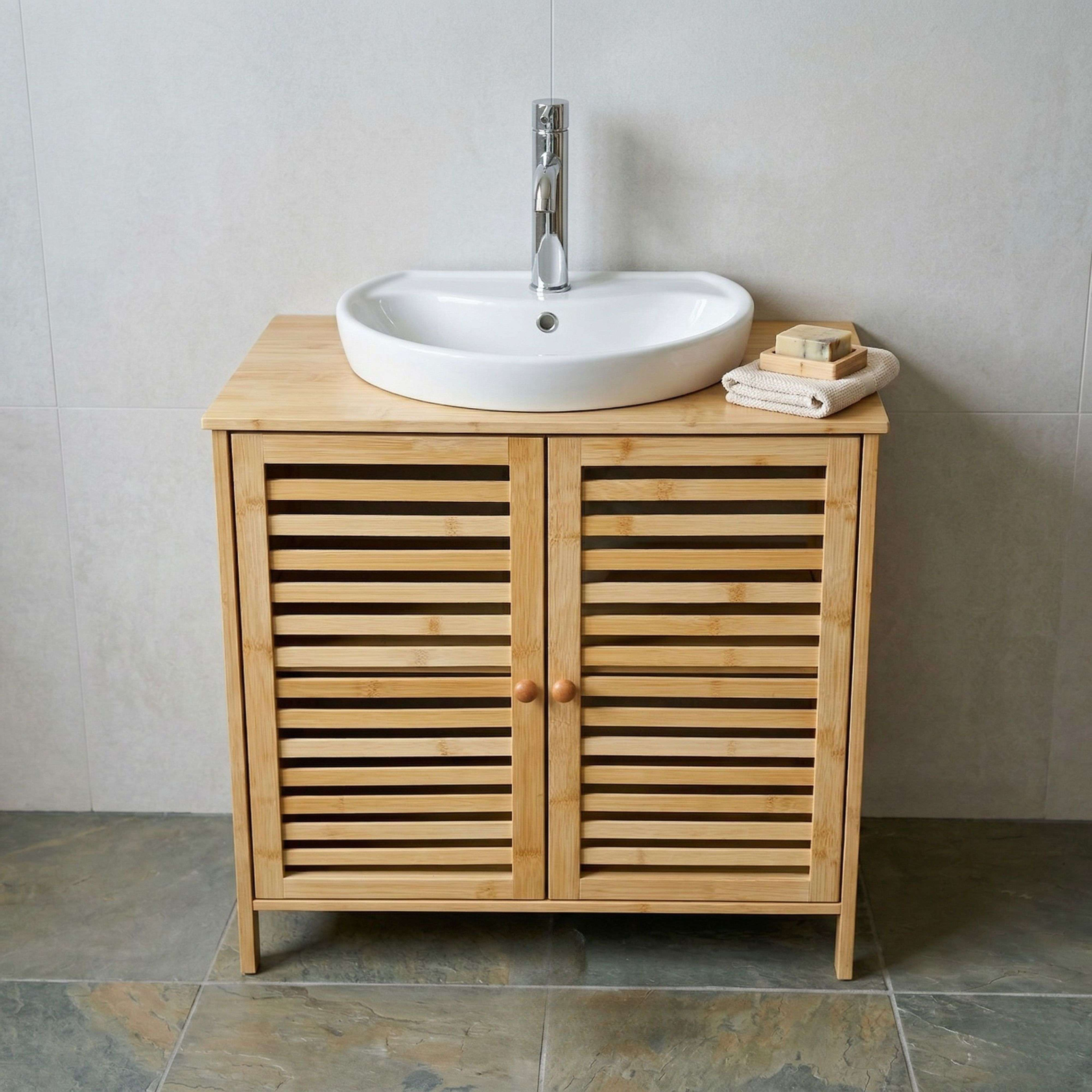 Un lavabo blanco sobre un mueble de madera con puertas de listones ante una pared de azulejos claros.
