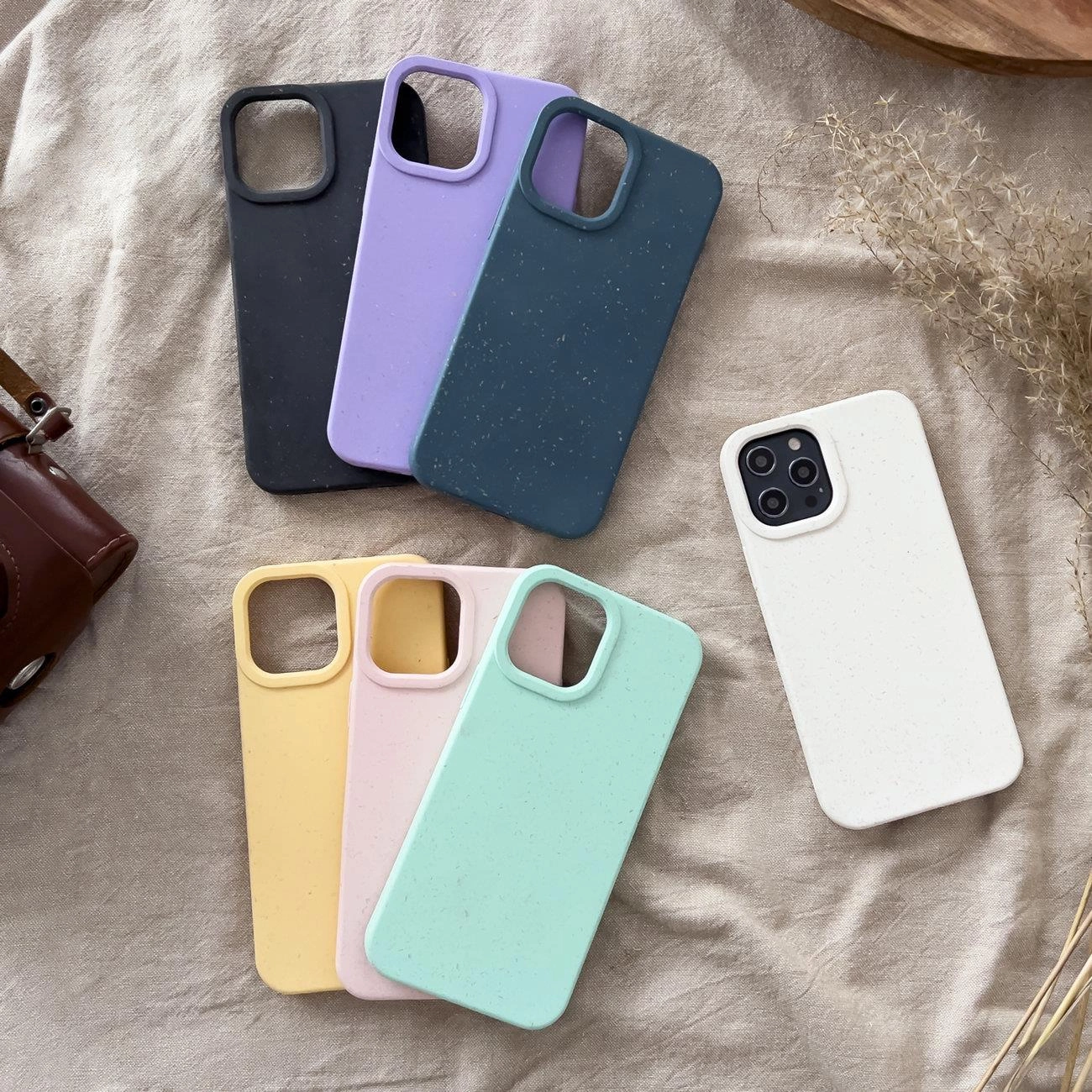 Diverse cover per cellulare colorate in tonalità pastello e scure su uno sfondo in tessuto beige.