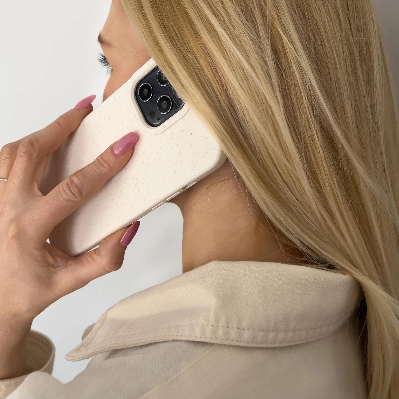Una donna bionda parla al telefono con uno smartphone beige su sfondo chiaro.
