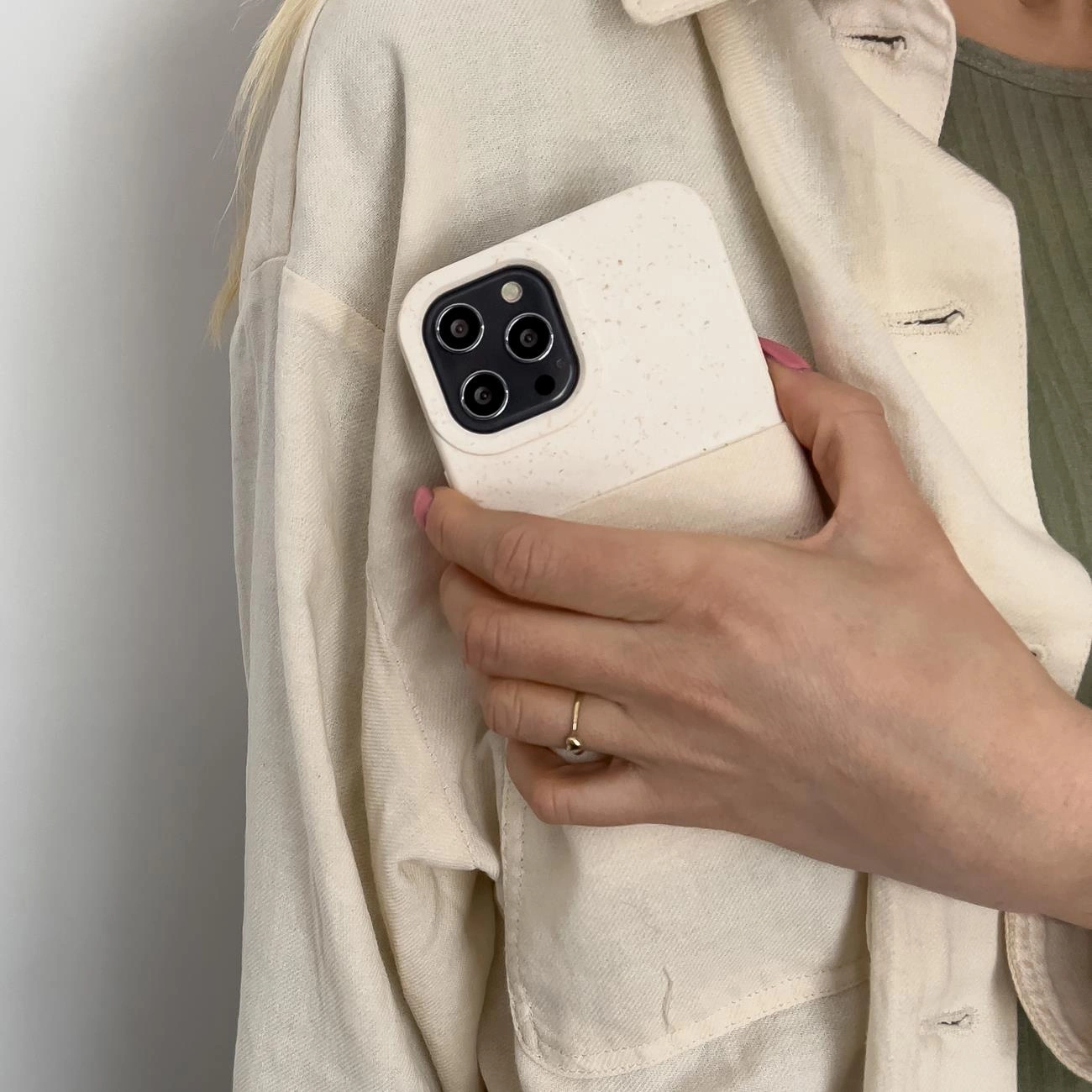 Una mano tiene uno smartphone con custodia beige, infilato nella tasca di una giacca chiara.