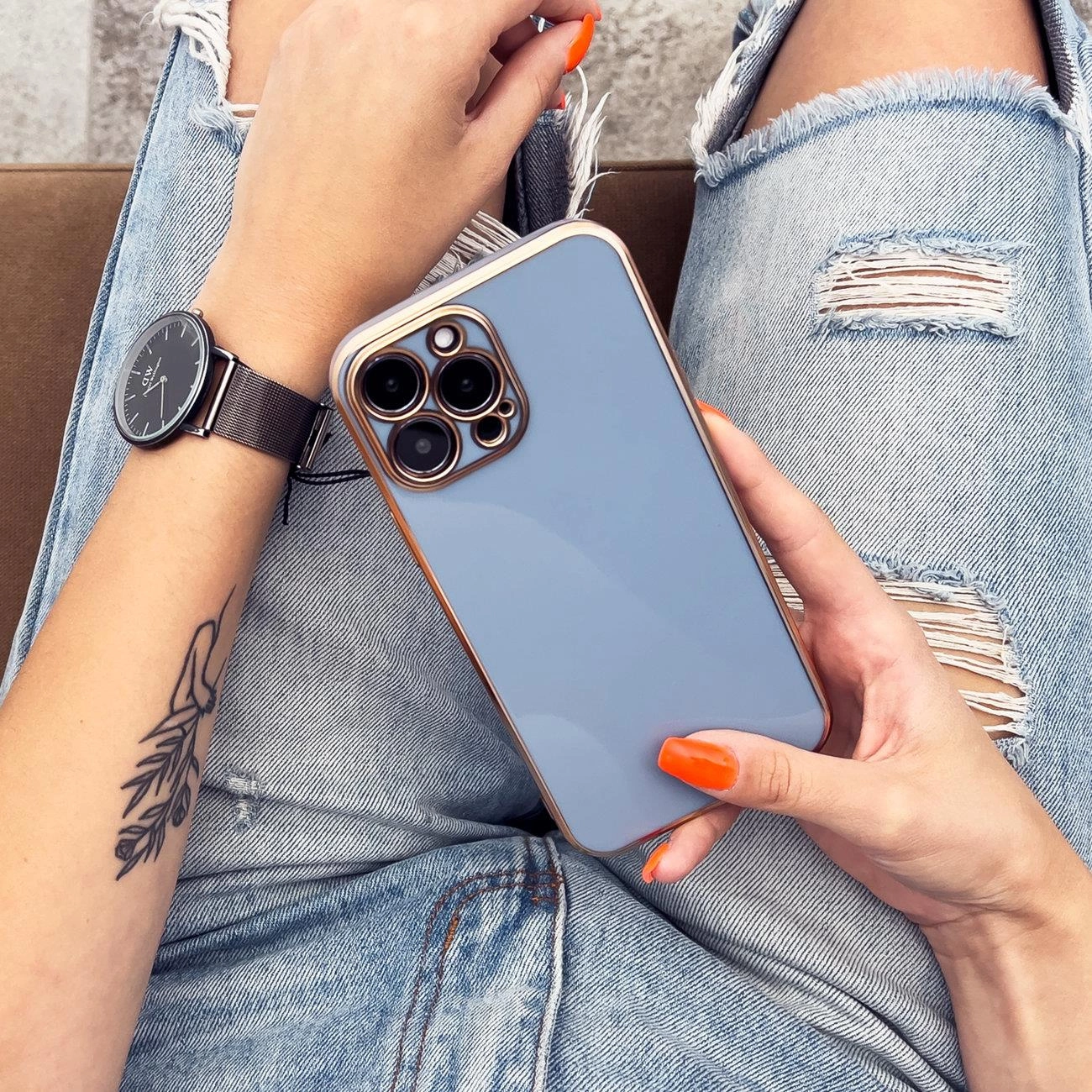 Persona con jeans strappati tiene uno smartphone azzurro con cornice dorata.