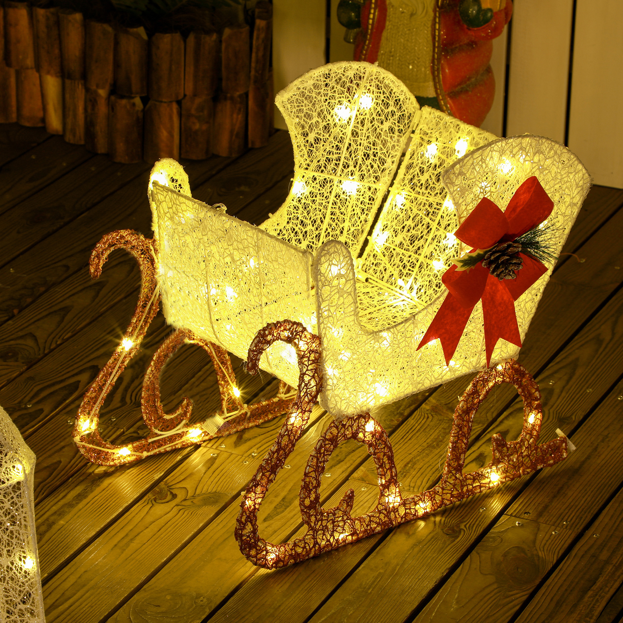 Un trineo de Navidad blanco e iluminado con lazos rojos en una cubierta de madera.