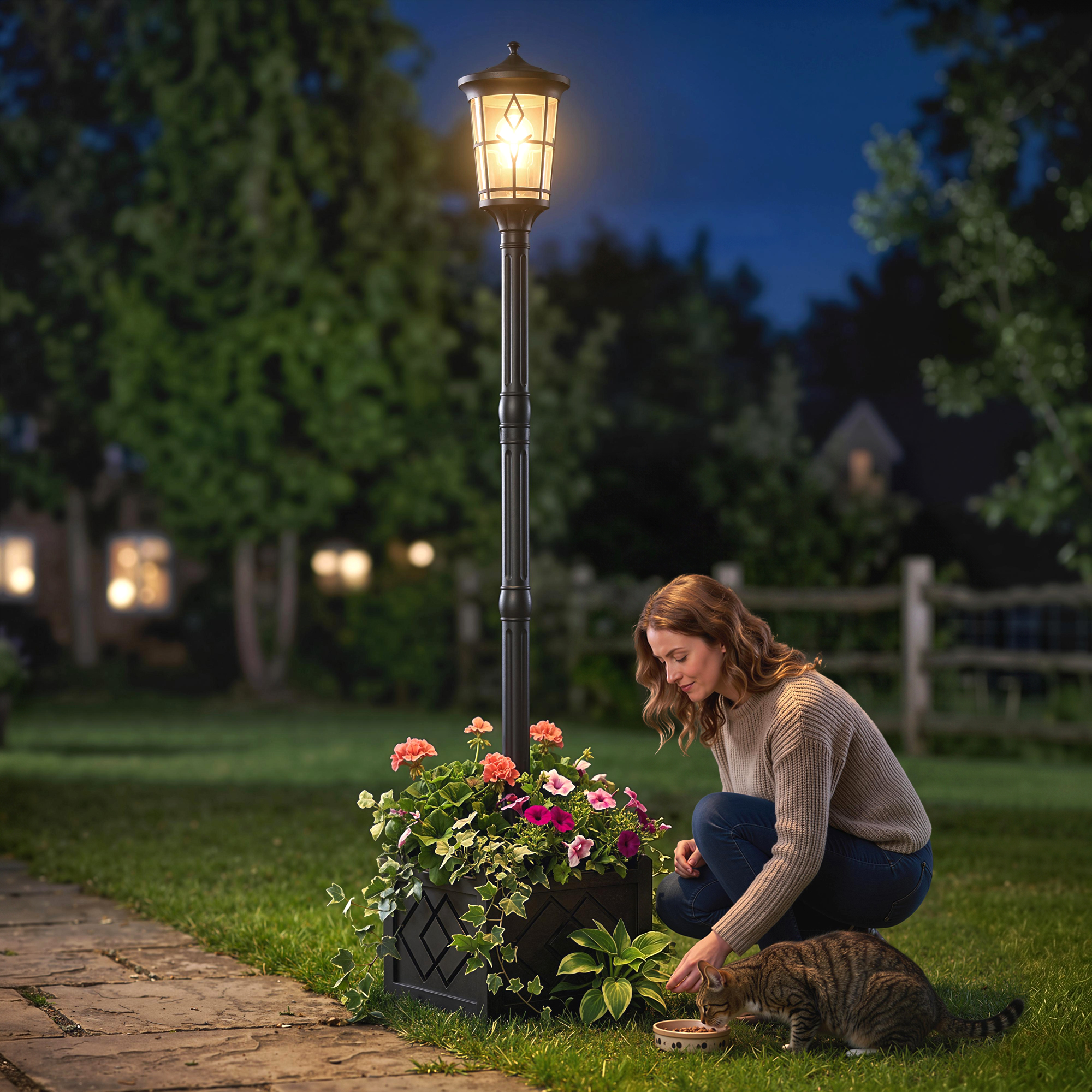 Una mujer se arrodilla junto a una farola iluminada en un jardín, alimentando a un gato.