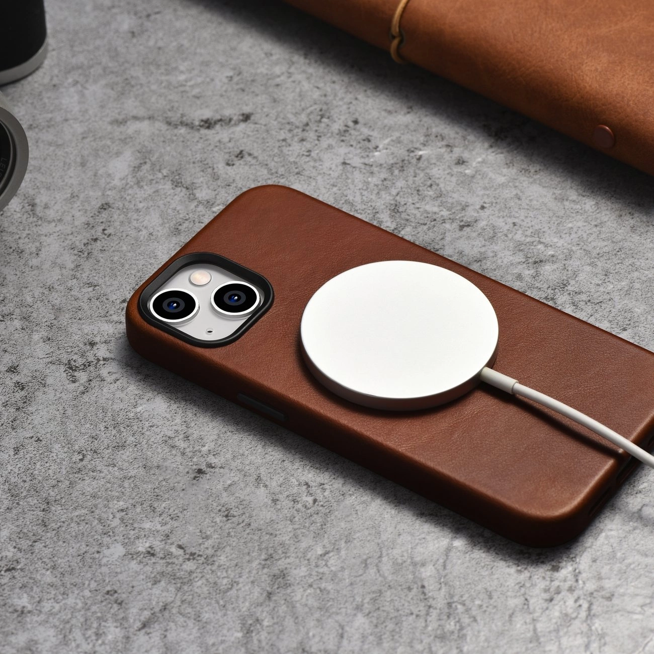 Una custodia per smartphone in pelle marrone con caricatore MagSafe su superficie grigia.