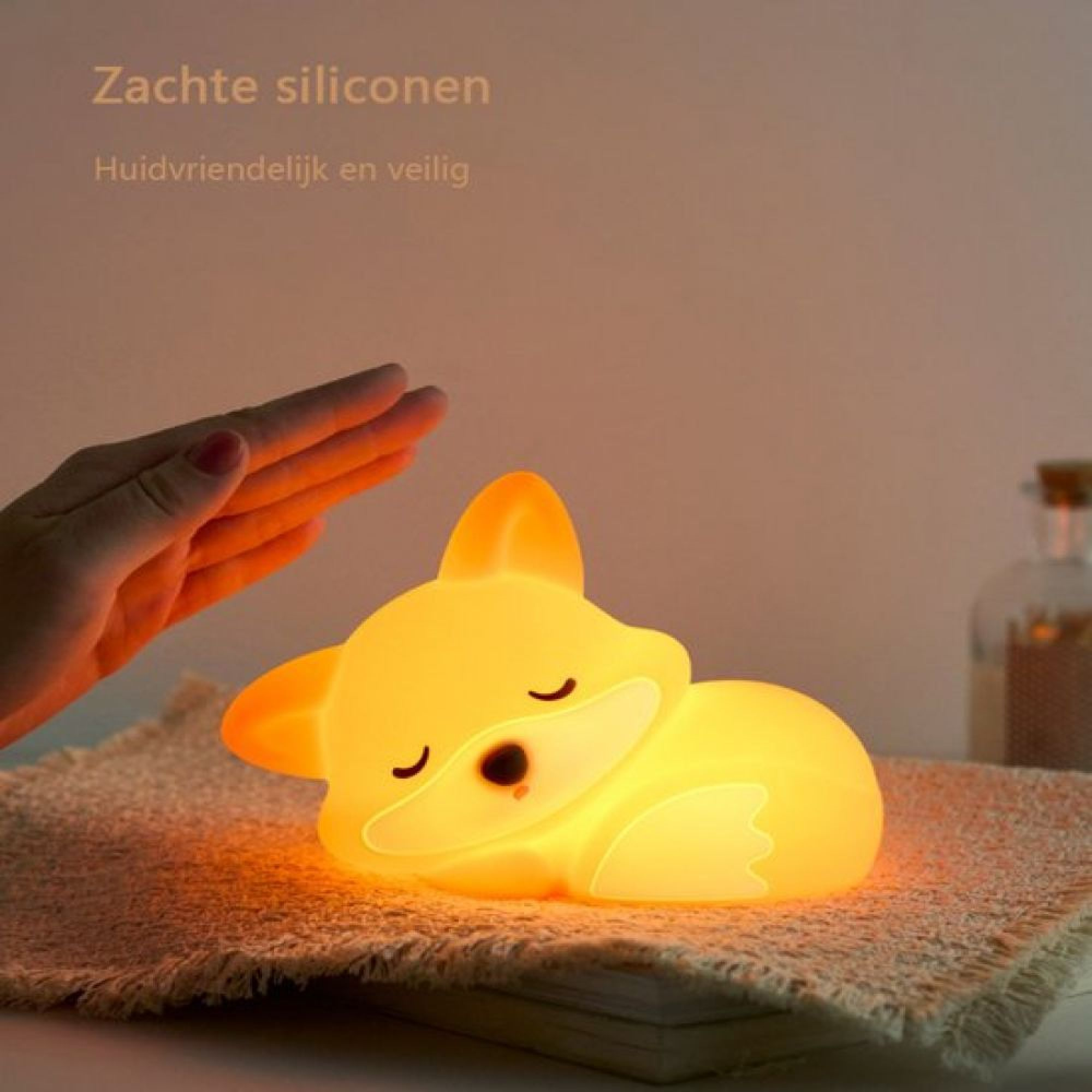 Eine Hand berührt sanft ein gelbes, schlafendes Fuchs-Nachtlicht aus Silikon auf einer Decke.