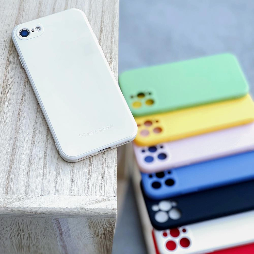 Uno smartphone bianco poggia su una superficie di legno, con una pila di cover colorate sullo sfondo.