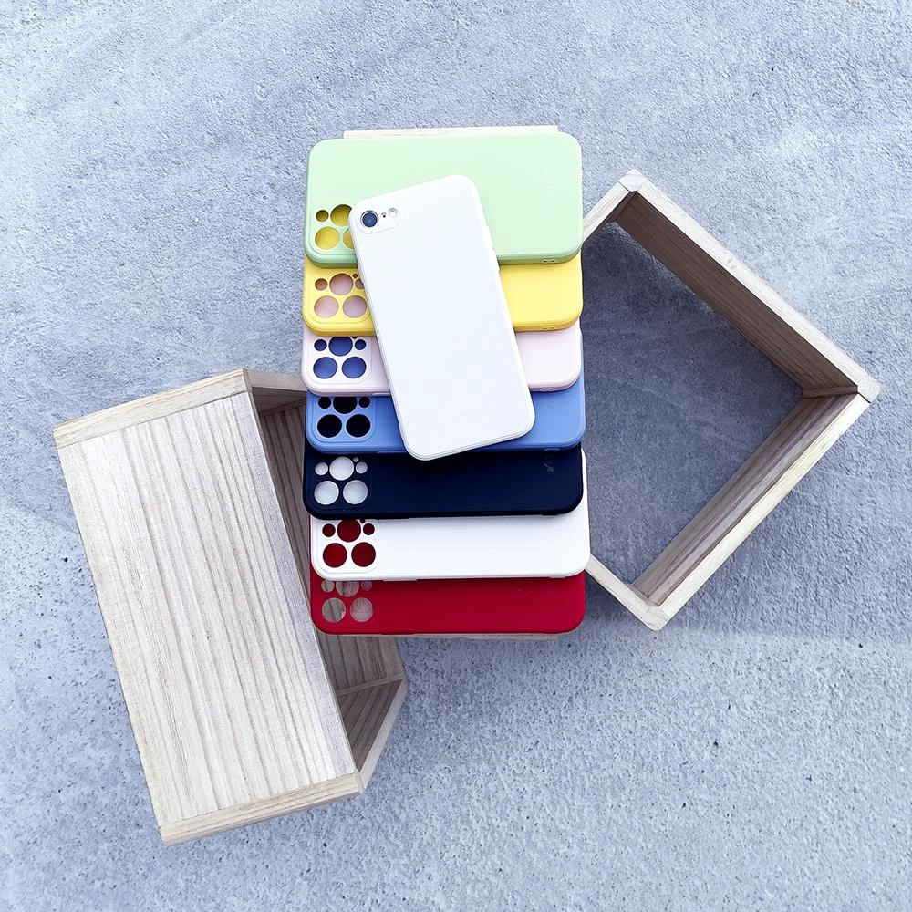 Una pila di custodie per telefoni colorate con un telefono bianco sopra, tra due scatole di legno su cemento.