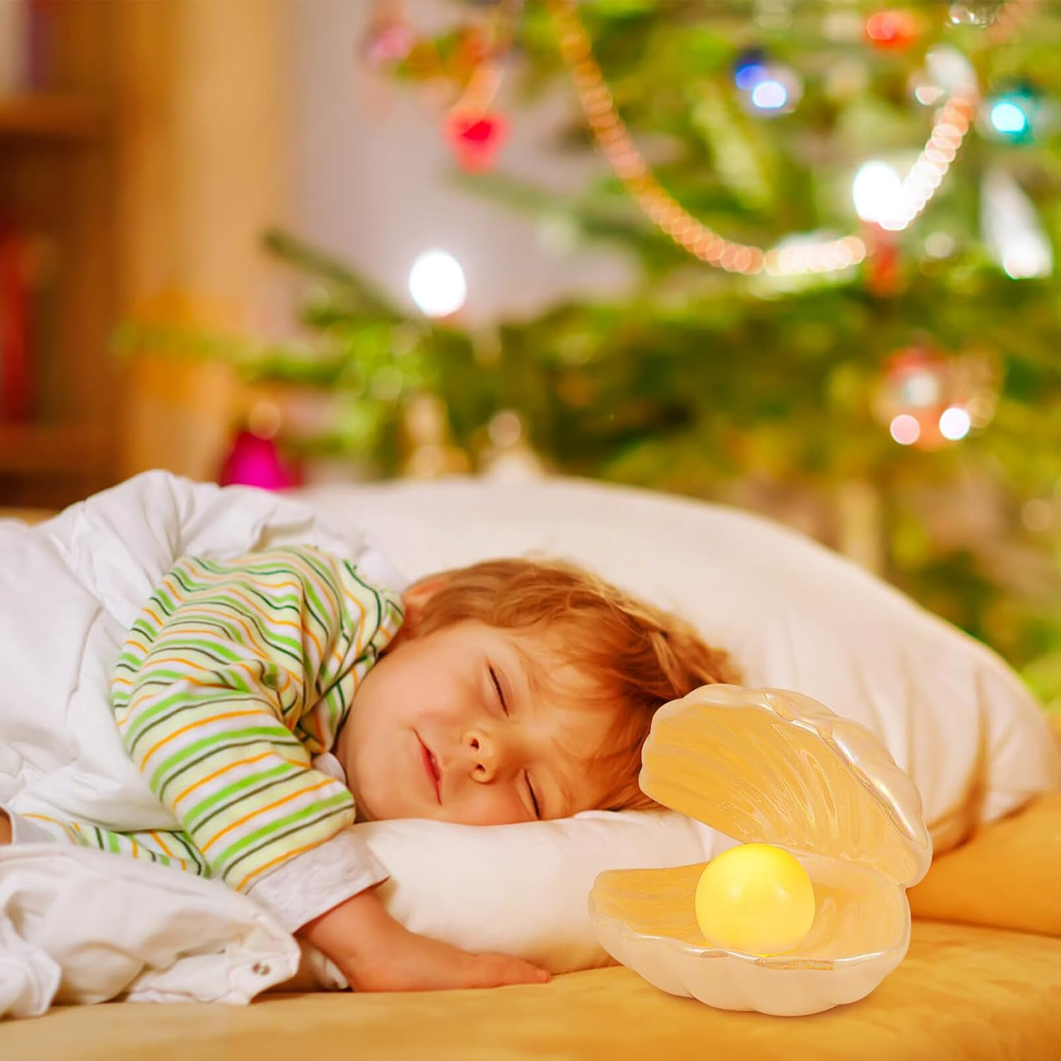 Ein Kleinkind schläft friedlich mit einem leuchtenden Muschelnachtlicht im Bett, im Hintergrund ein Weihnachtsbaum.