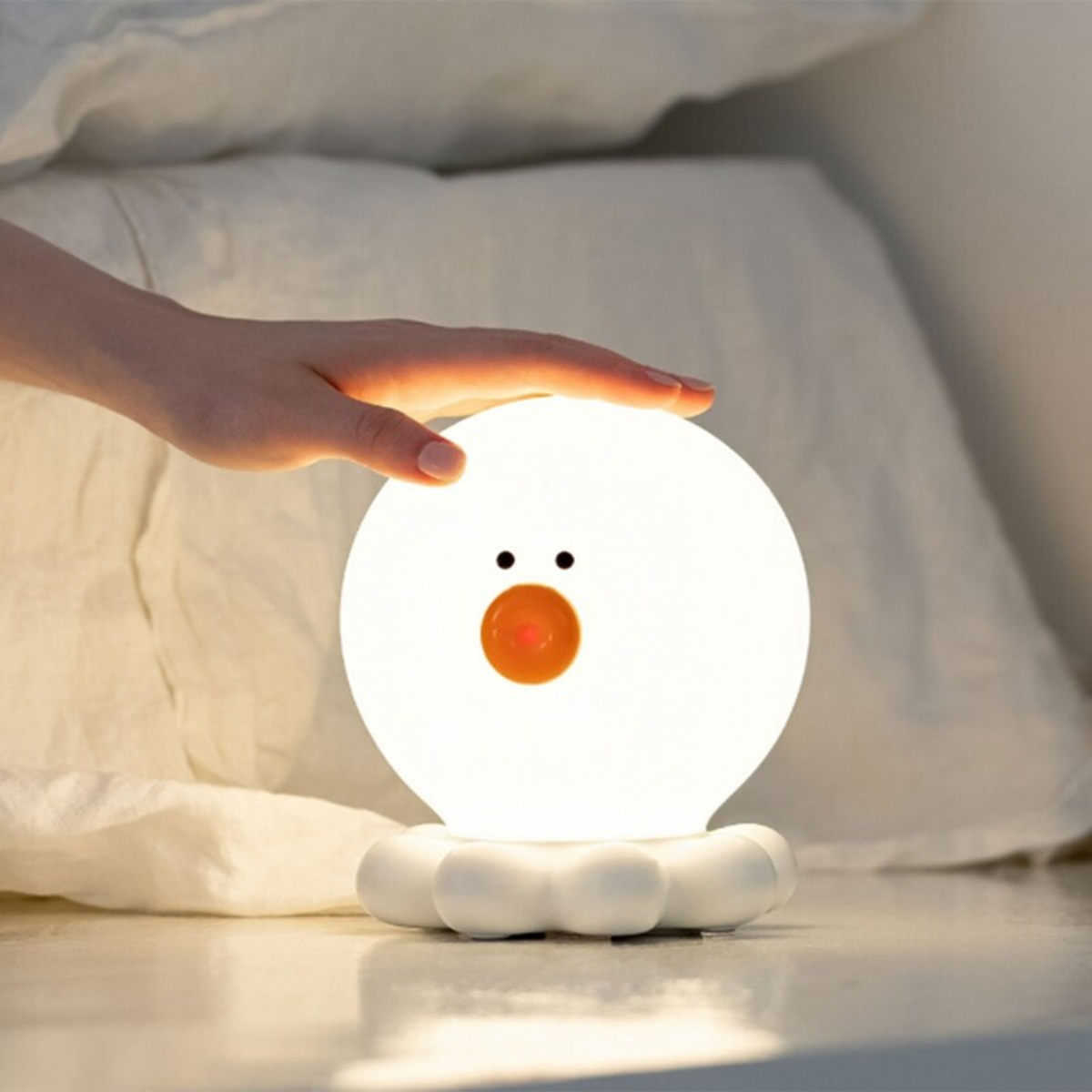 Eine Hand berührt eine kugelförmige, niedliche Nachtlampe mit Entengesicht und Pfotenbasis.