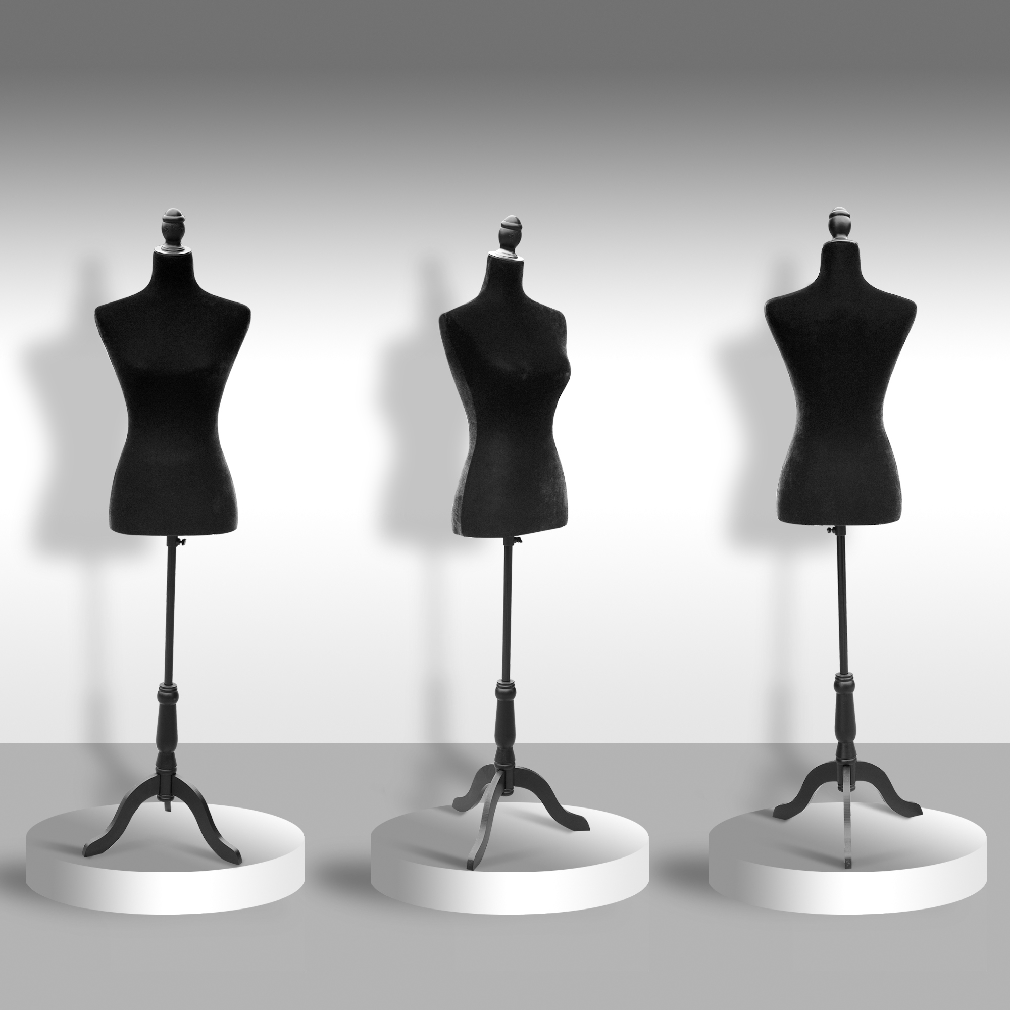 Tres maniquíes negros en soportes contra un fondo de estudio gris y blanco.