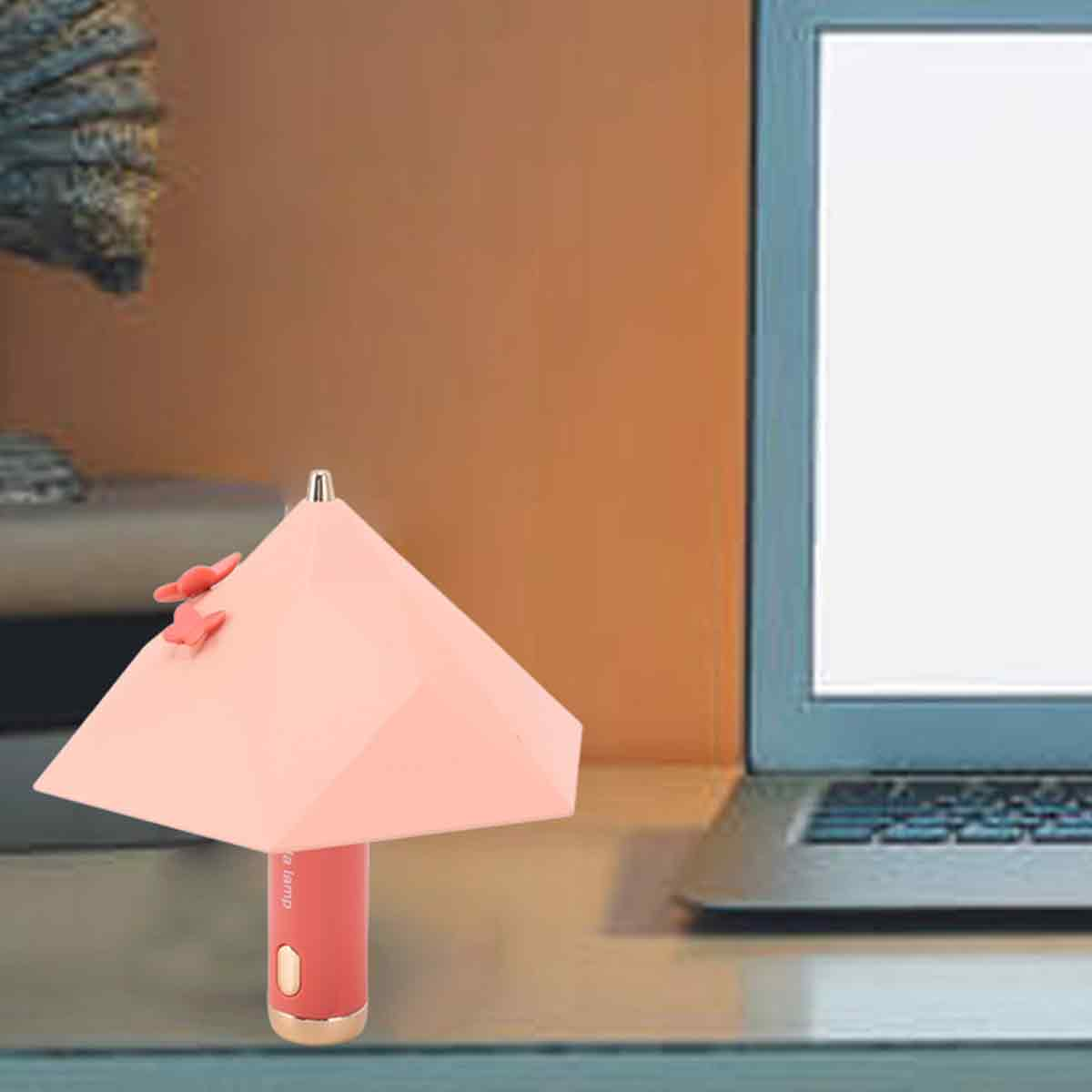 Eine pinke, kegelförmige Tischlampe mit Blumenverzierung steht auf einem Schreibtisch neben einem Laptop.