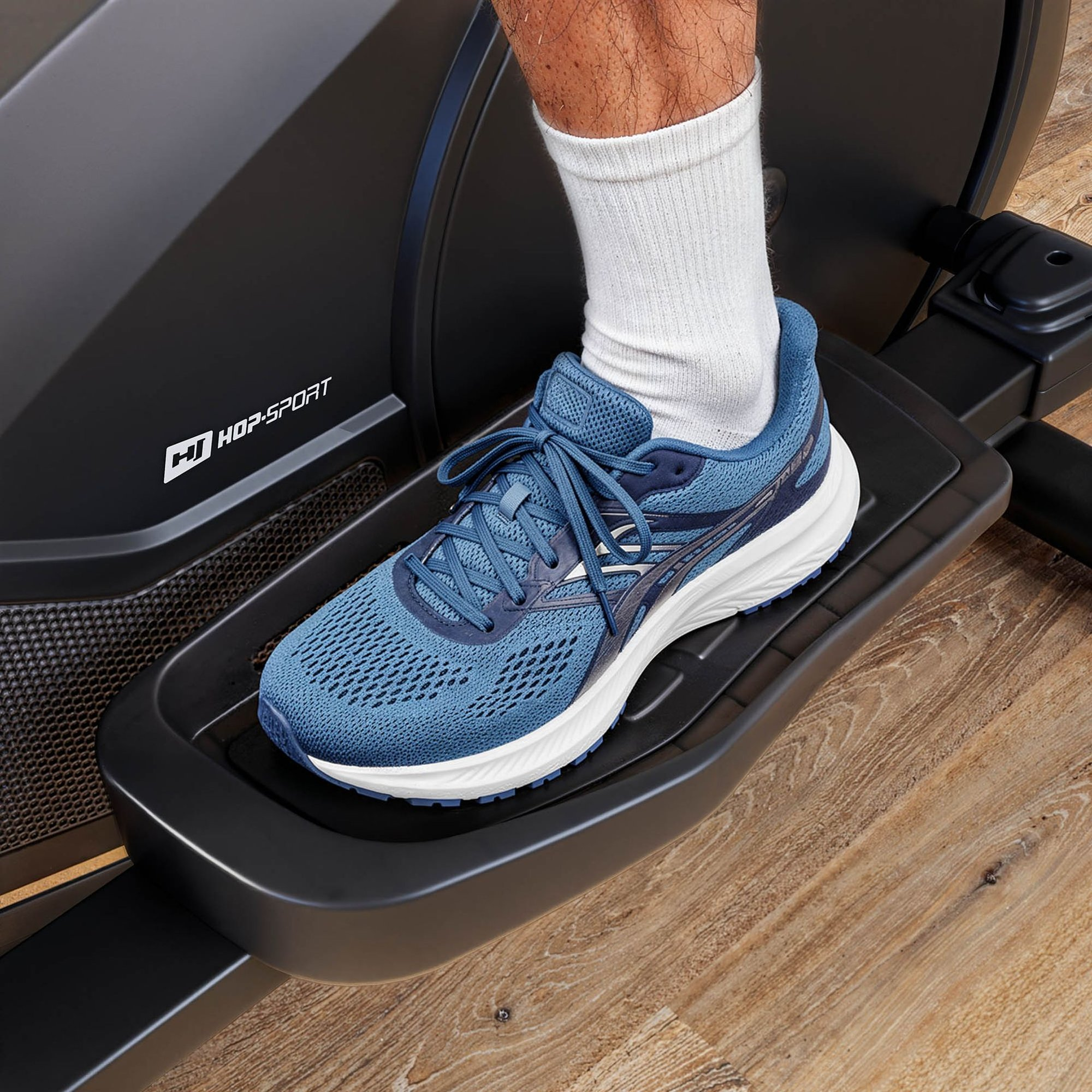 Der Fuß einer Person in einem blauen Sneaker und weißer Socke auf dem Pedal eines Crosstrainers.