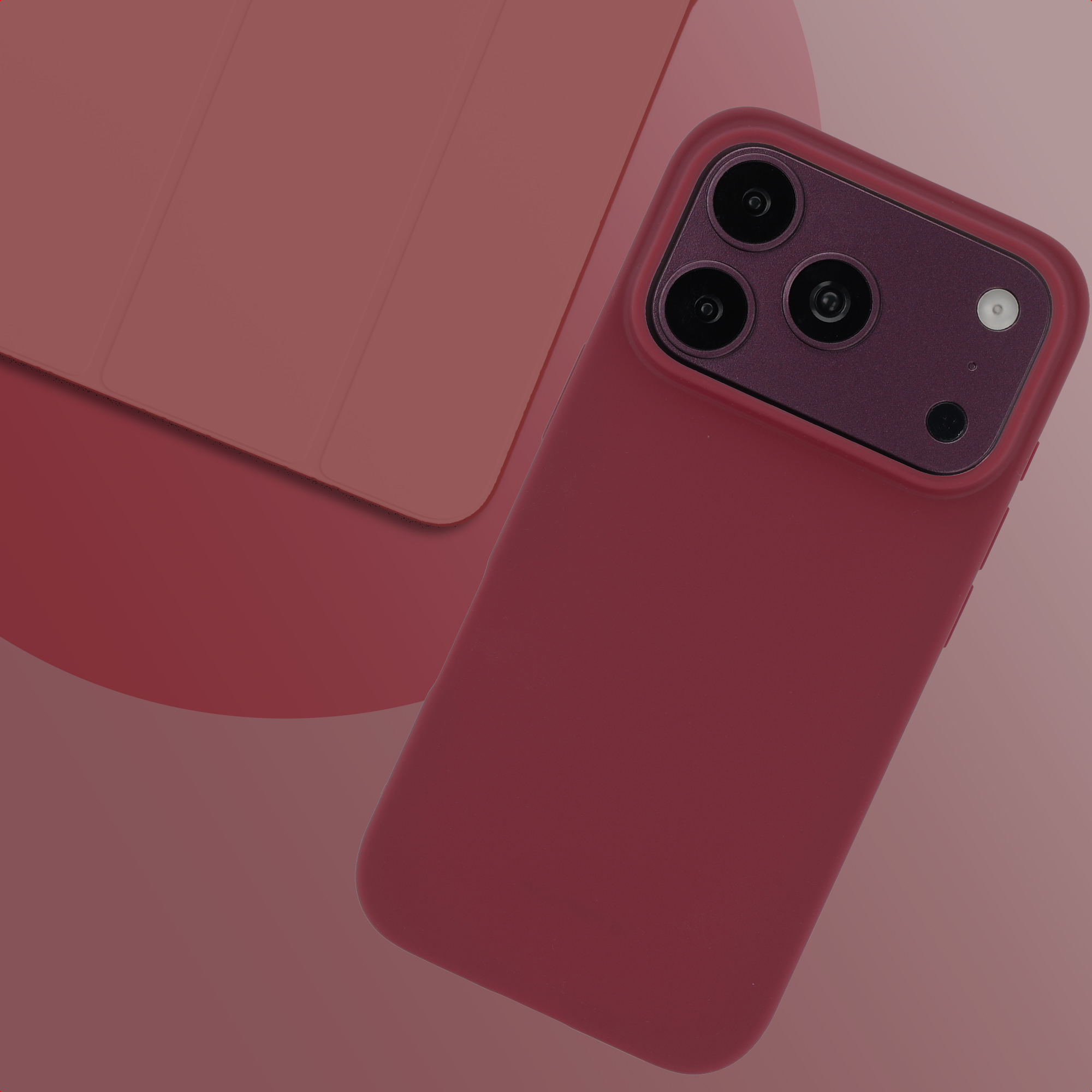 Een donkerrode smartphone in een bijpassend hoesje ligt op een roze oppervlak naast een rode hoes.