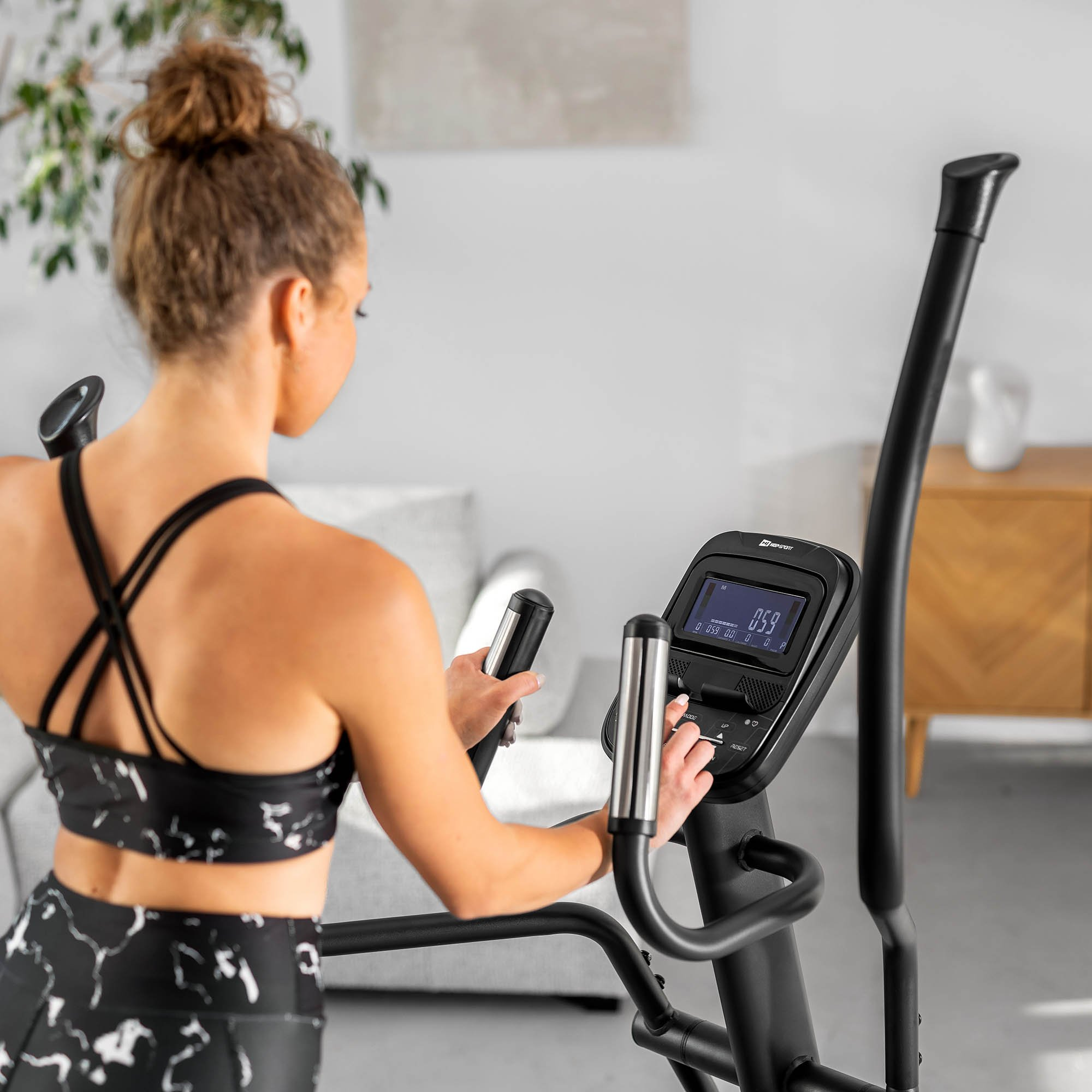 Eine Frau in Sportkleidung trainiert zu Hause an einem Crosstrainer.