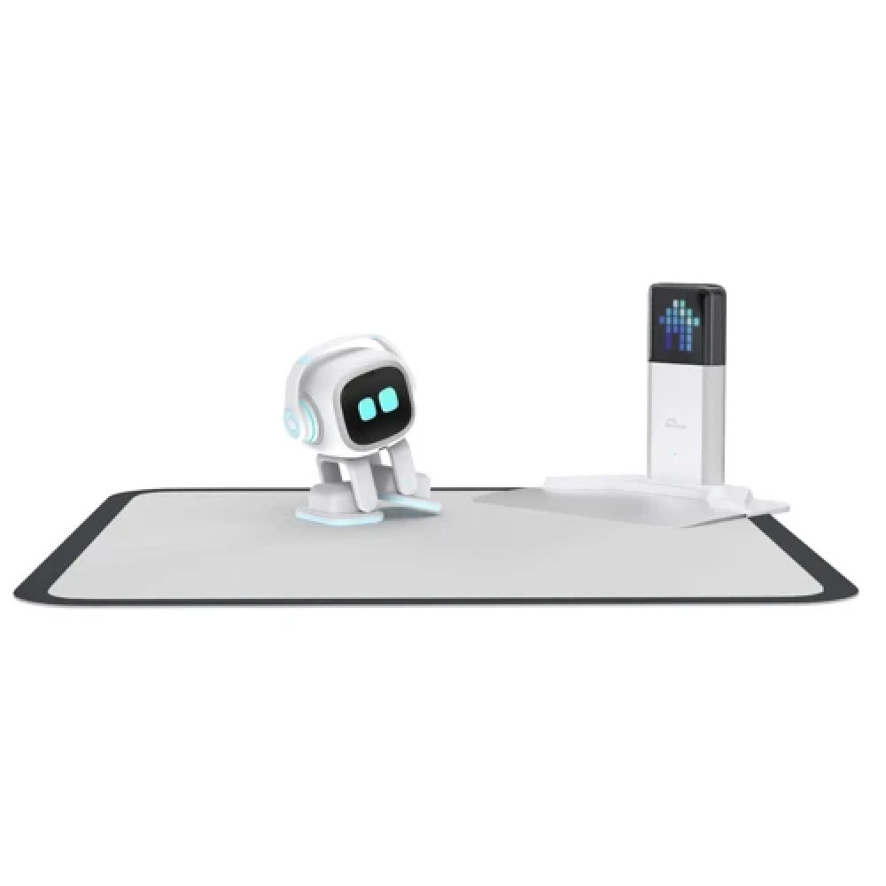 Açık mavi gözlü ve kulaklıklı küçük beyaz bir robot, şarj istasyonunun yanında gri bir mat üzerinde duruyor.