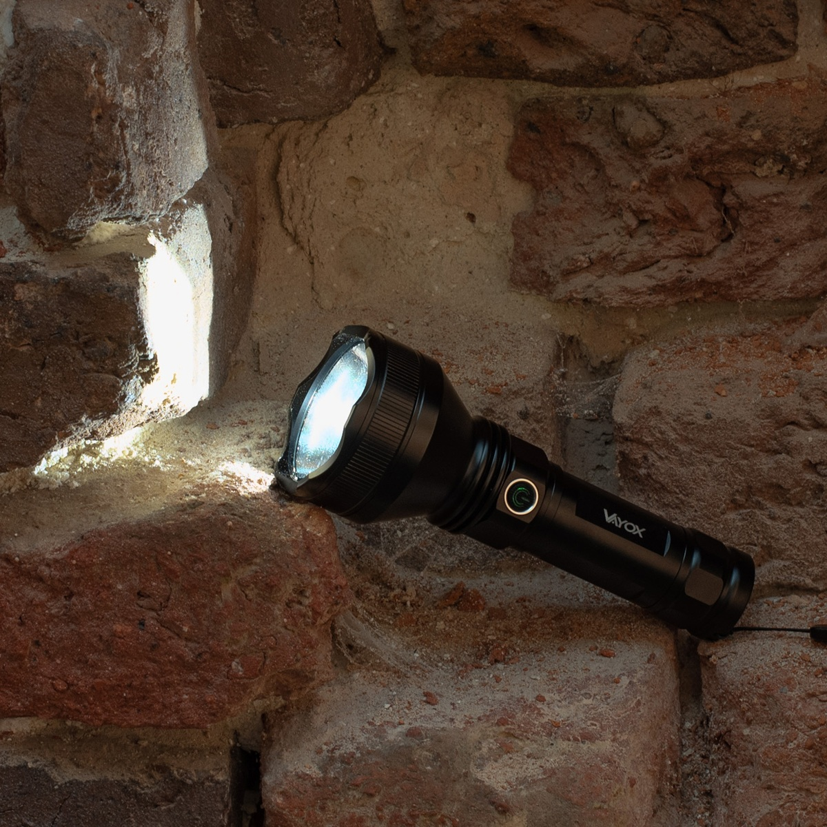 Eine schwarze Taschenlampe leuchtet gegen eine alte Backsteinwand.