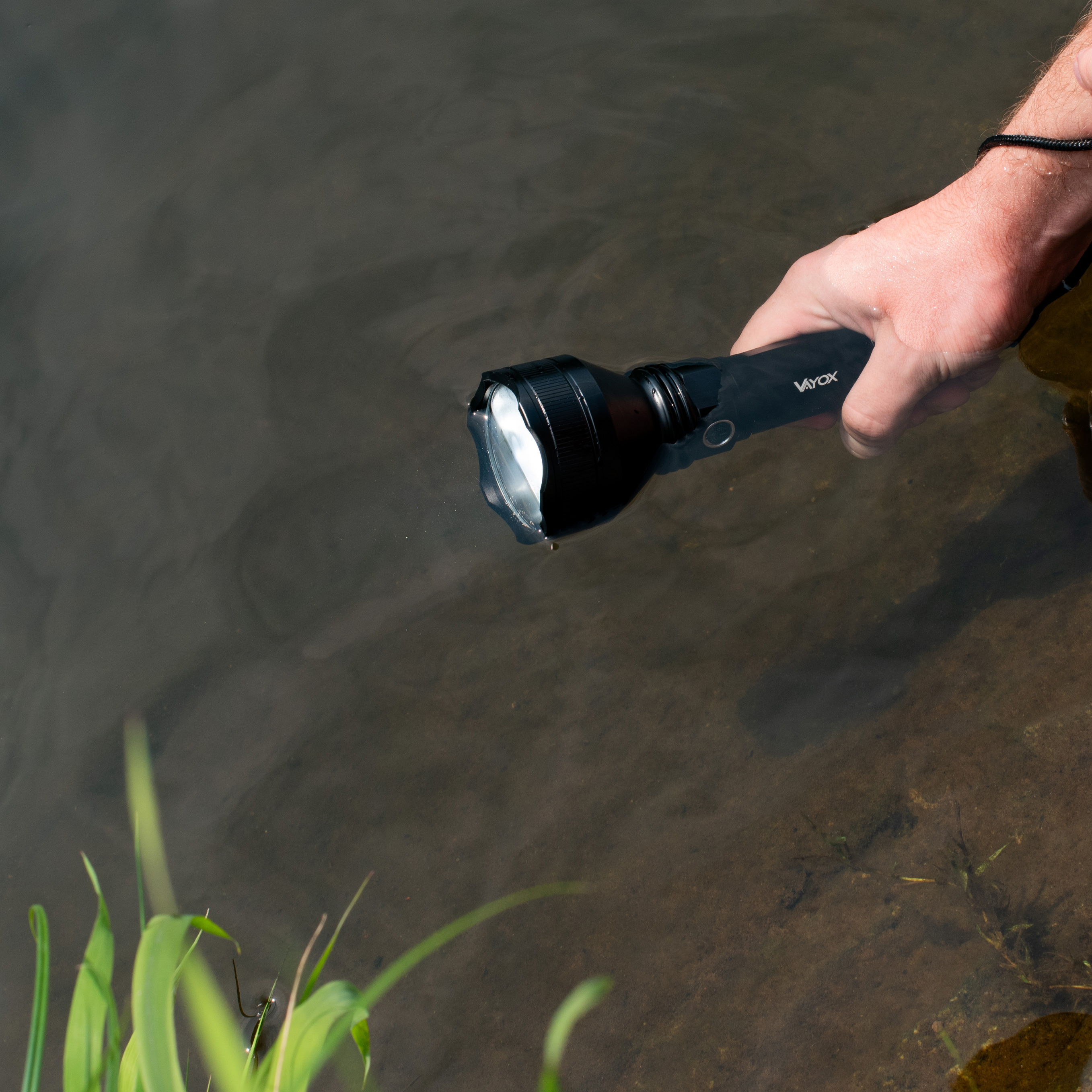 Eine Hand hält eine schwarze Vayox-Taschenlampe, die teilweise in klarem Wasser eingetaucht ist.