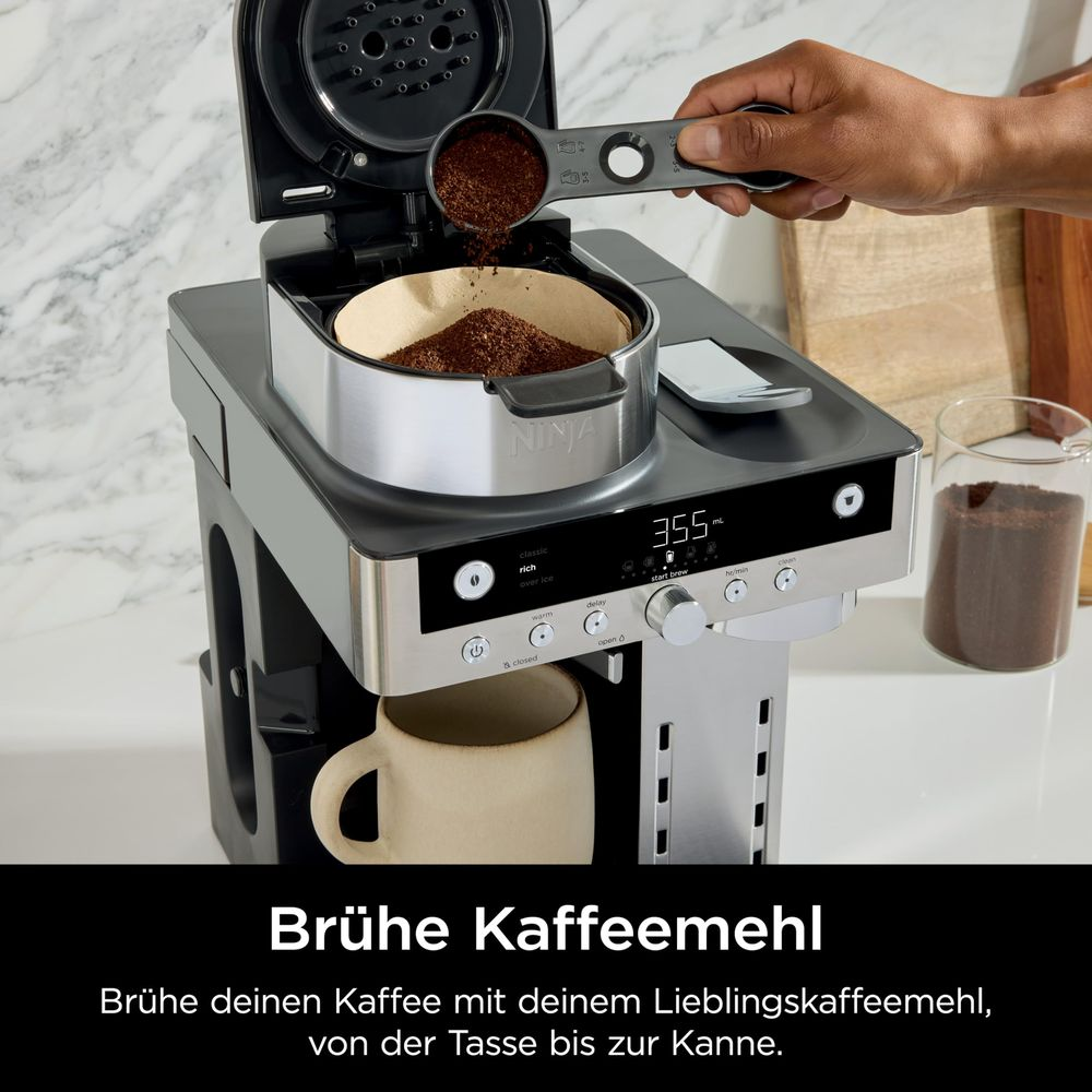 Una mano versa il caffè macinato con un cucchiaio dosatore nel filtro di una macchina da caffè Ninja.