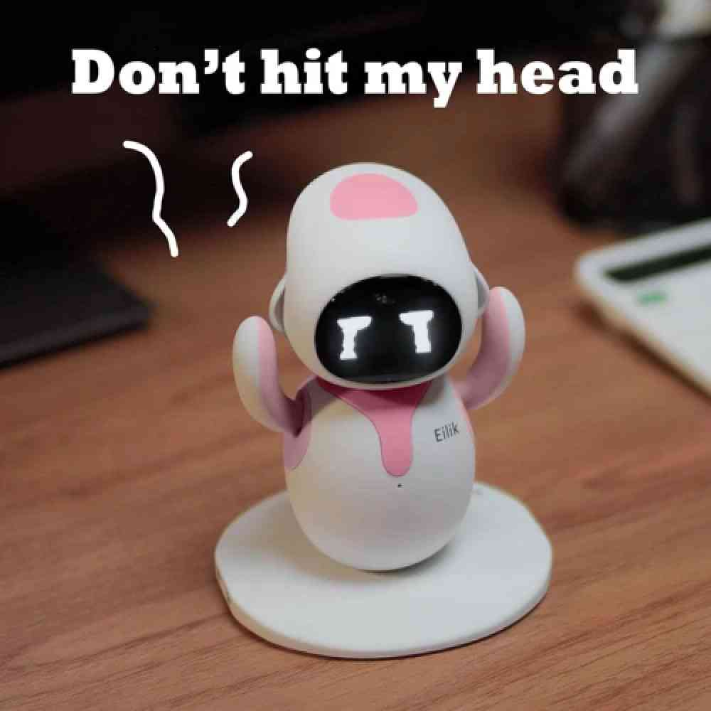Masada üzgün yüzlü beyaz ve pembe bir robot, üzerinde "Don't hit my head" yazısı var.