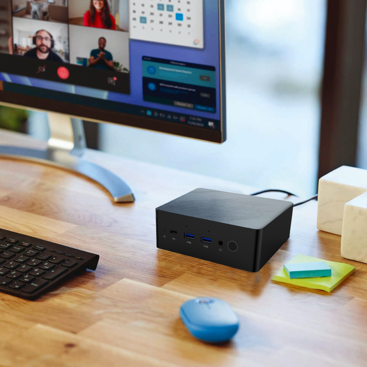 Czarny mini PC na drewnianym biurku z monitorem, klawiaturą i niebieską myszą.