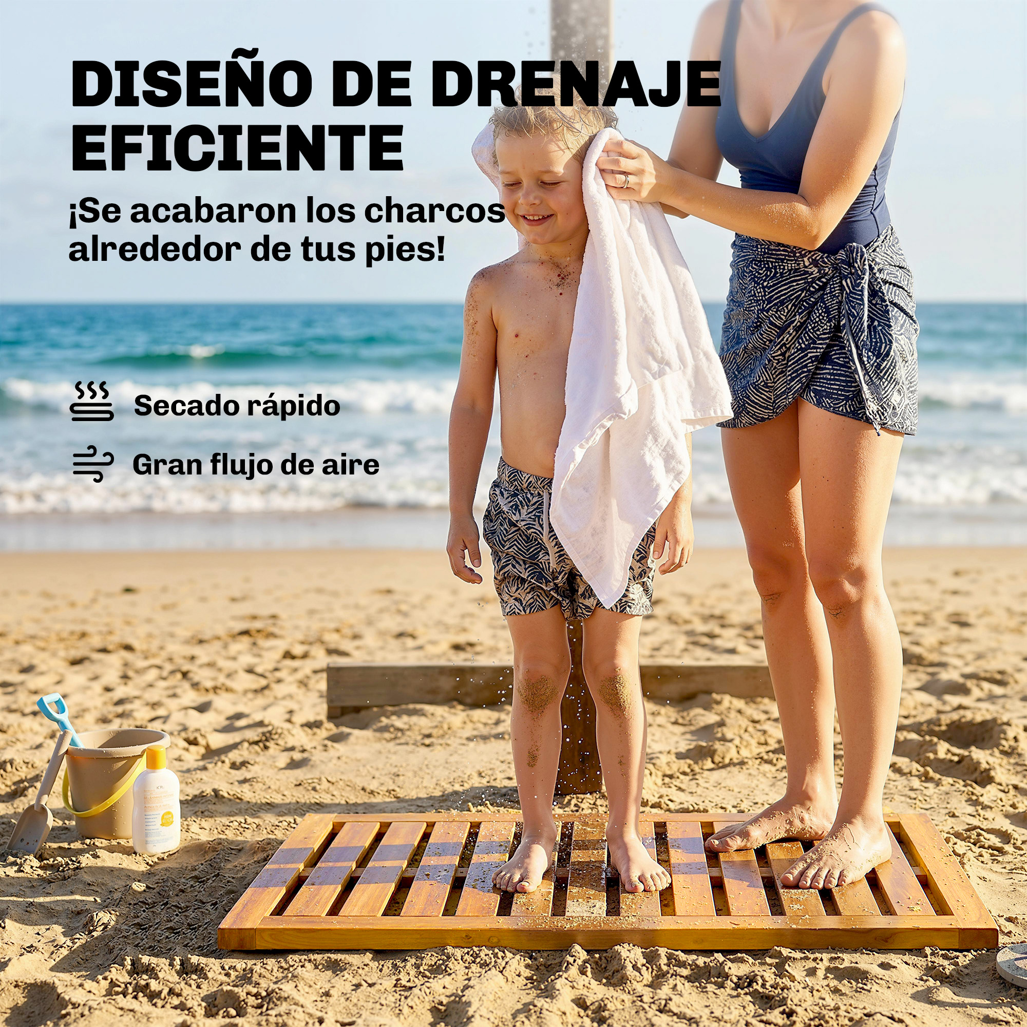 Una mujer seca a un niño sonriente con una toalla en una alfombrilla de ducha de madera en la playa.