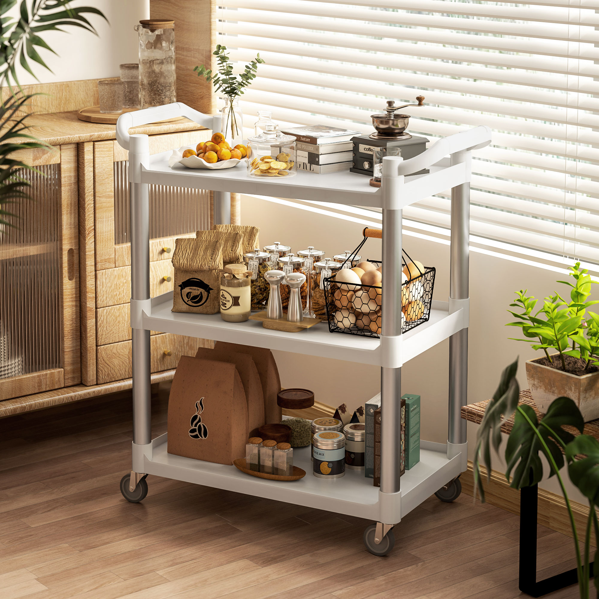 Un carrito blanco de tres niveles con frascos de comida, huevos, café y fruta en una cocina soleada.