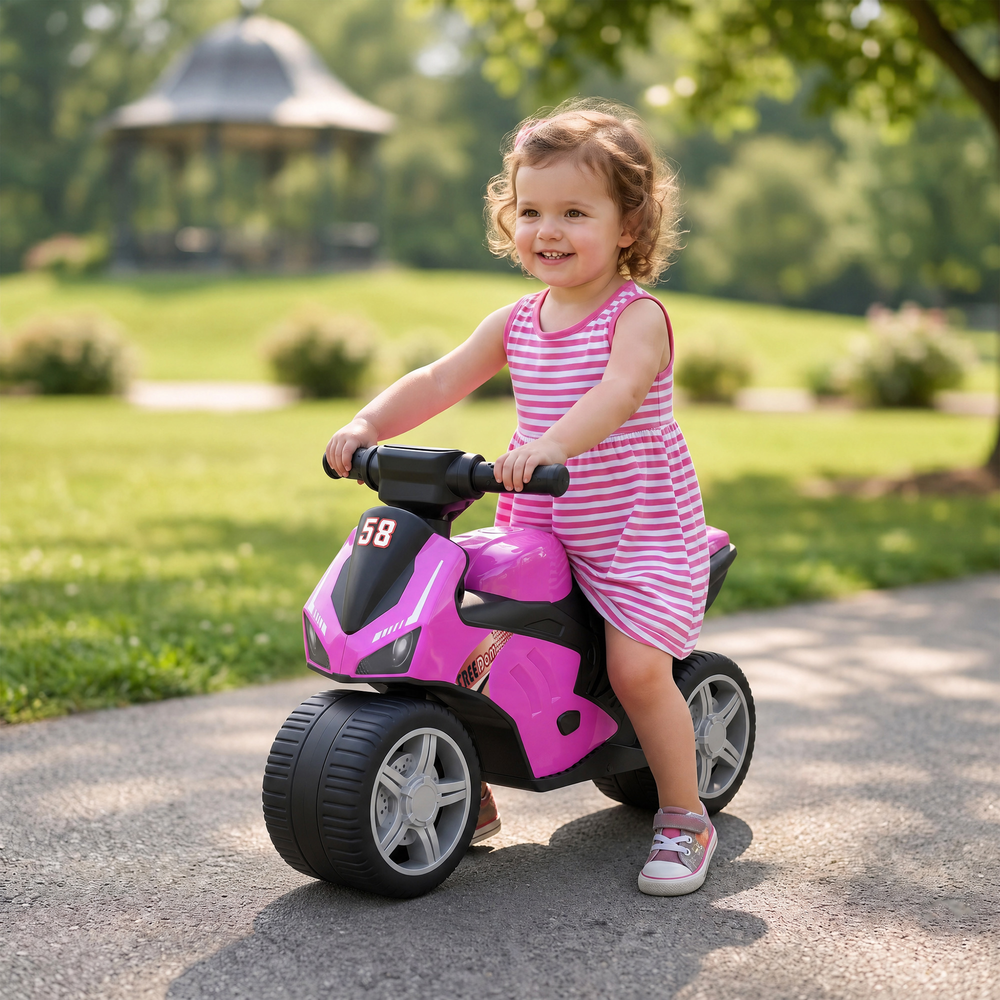 Un niño pequeño sonriente monta en una moto de juguete rosa por un sendero pavimentado.