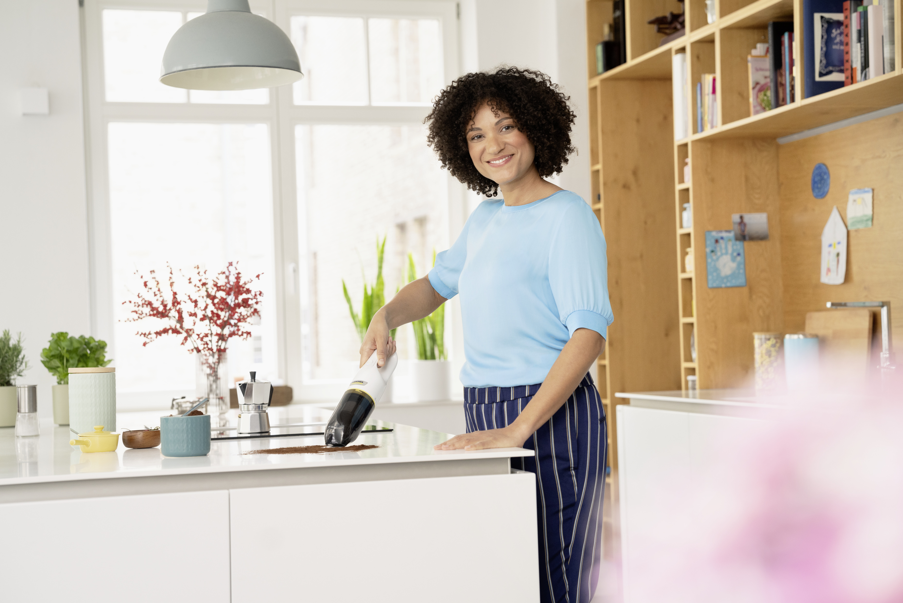 Een vrouw in een blauw shirt gebruikt een handstofzuiger op een wit aanrecht.
