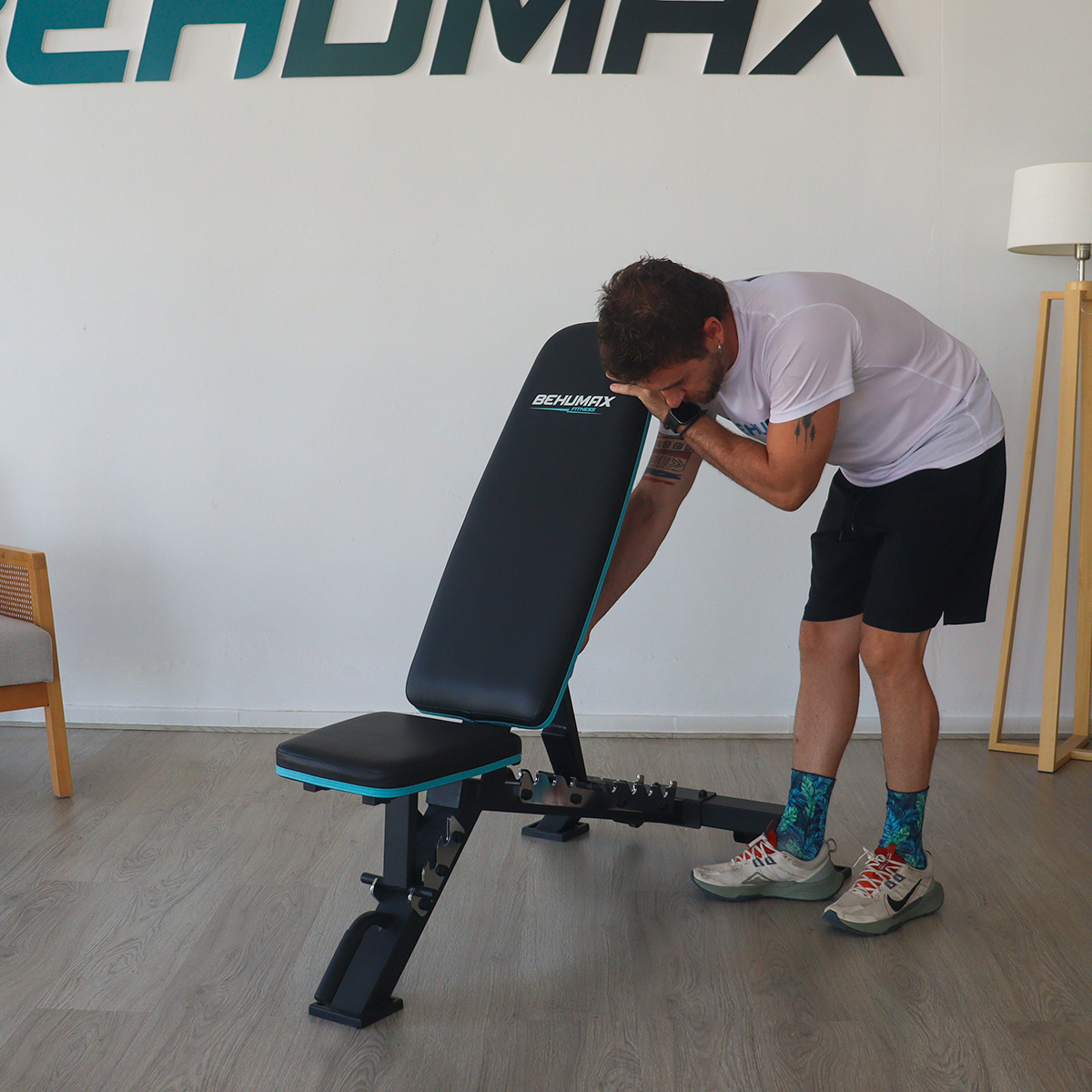 Un hombre ajusta un banco de fitness negro y azul en un interior con suelo de madera.