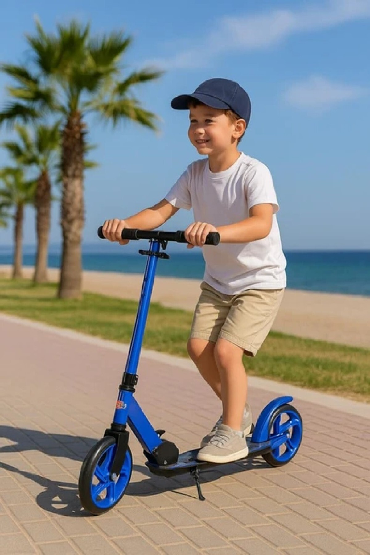 Şapkalı ve beyaz tişörtlü bir çocuk, palmiyeli sahil gezinti yolunda mavi scooter sürüyor.
