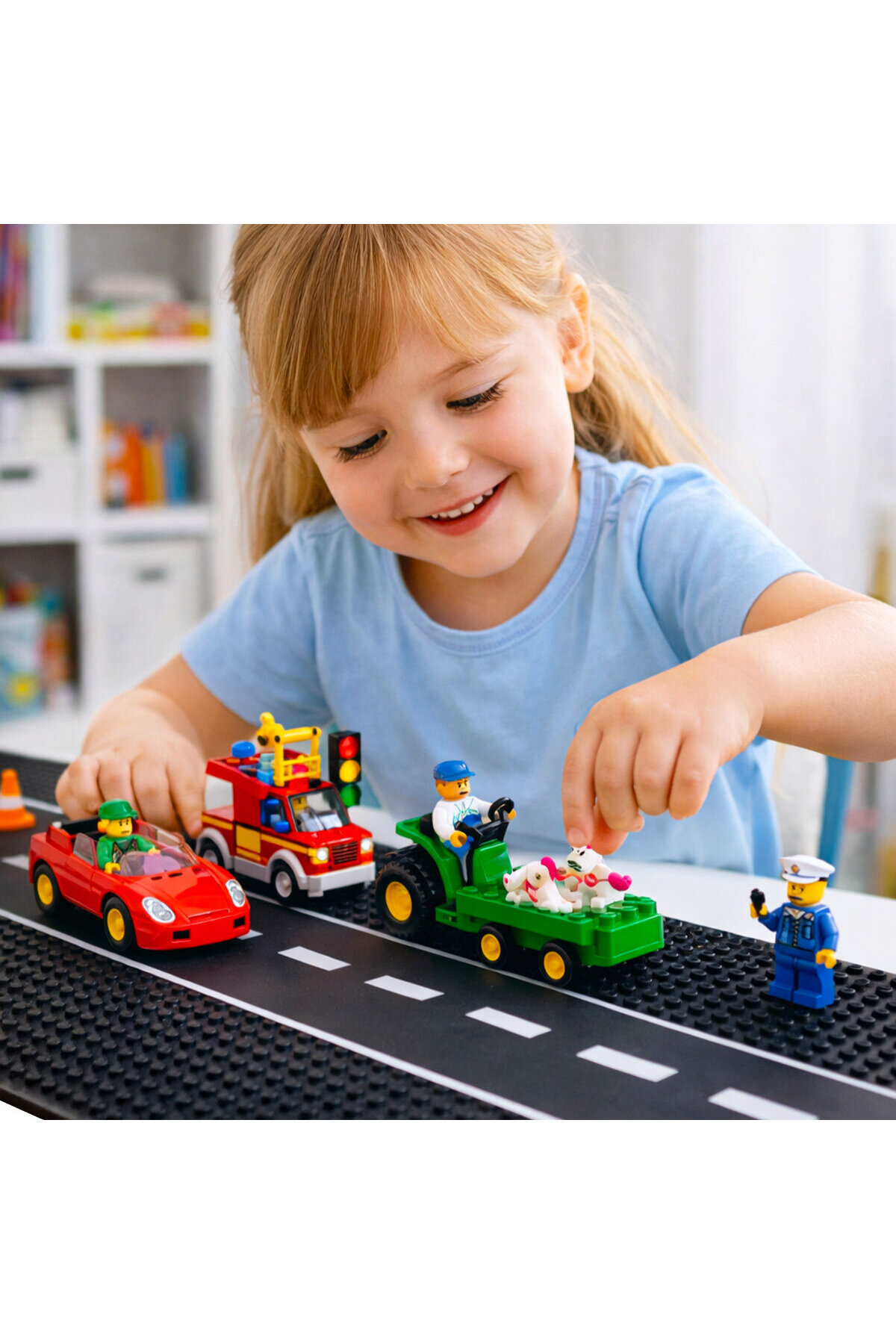 Küçük bir kız, oyuncak bir yolda renkli Lego Duplo arabaları ve figürleriyle oynarken gülümsüyor.
