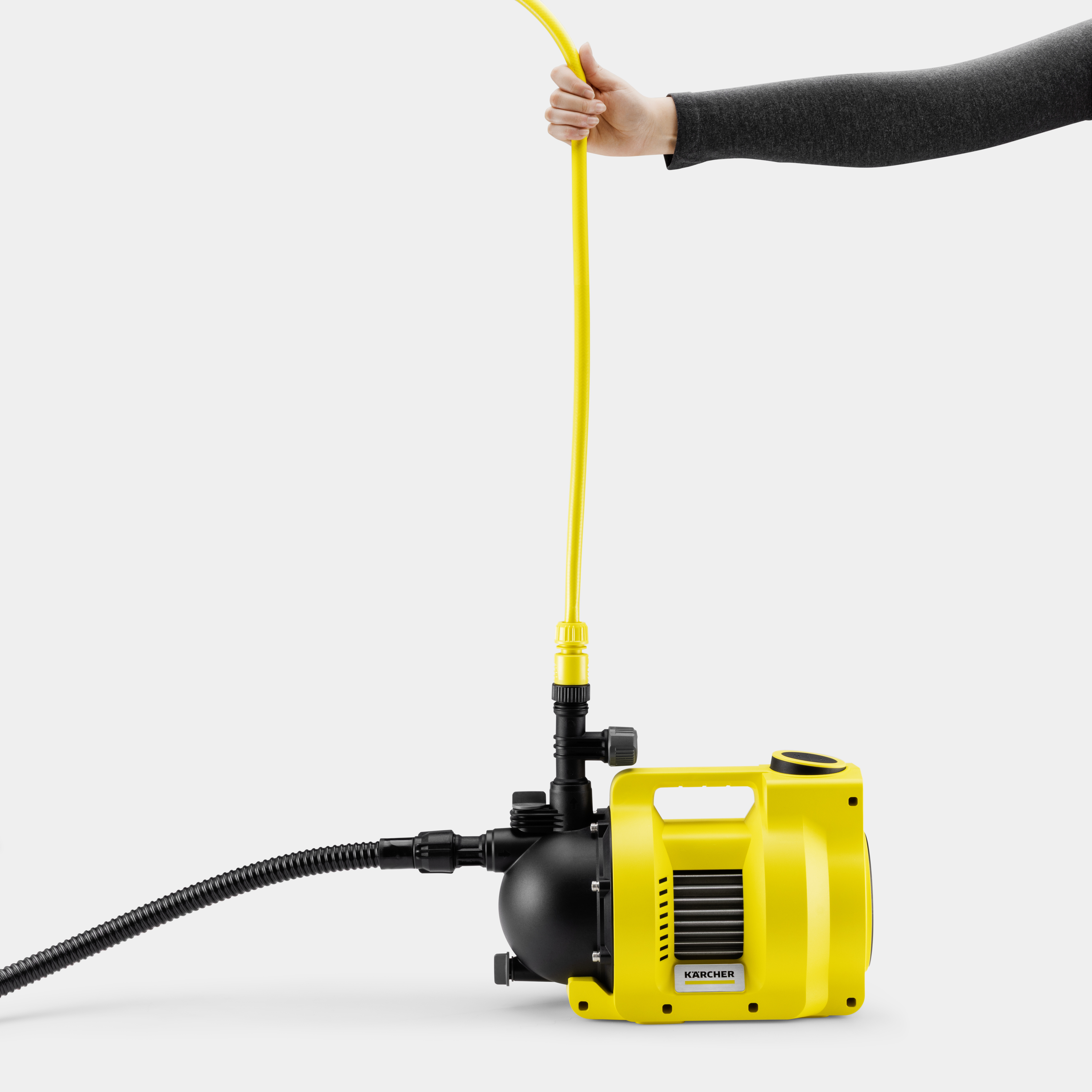 Una mano regge un tubo giallo collegato a una pompa da giardino Kärcher gialla e nera su sfondo bianco.