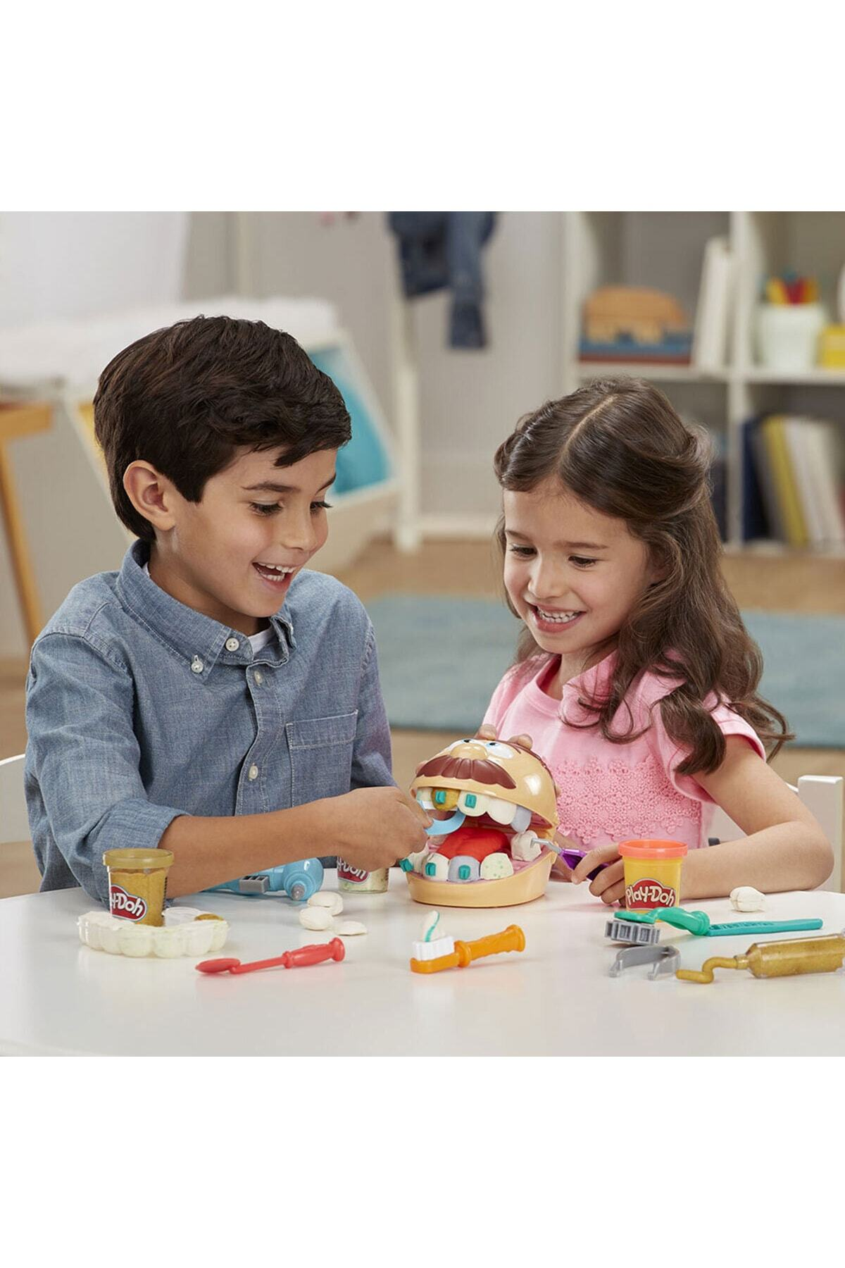 Bir kız ve erkek çocuk masada Play-Doh dişçi oyuncak setiyle neşeyle oynuyor.