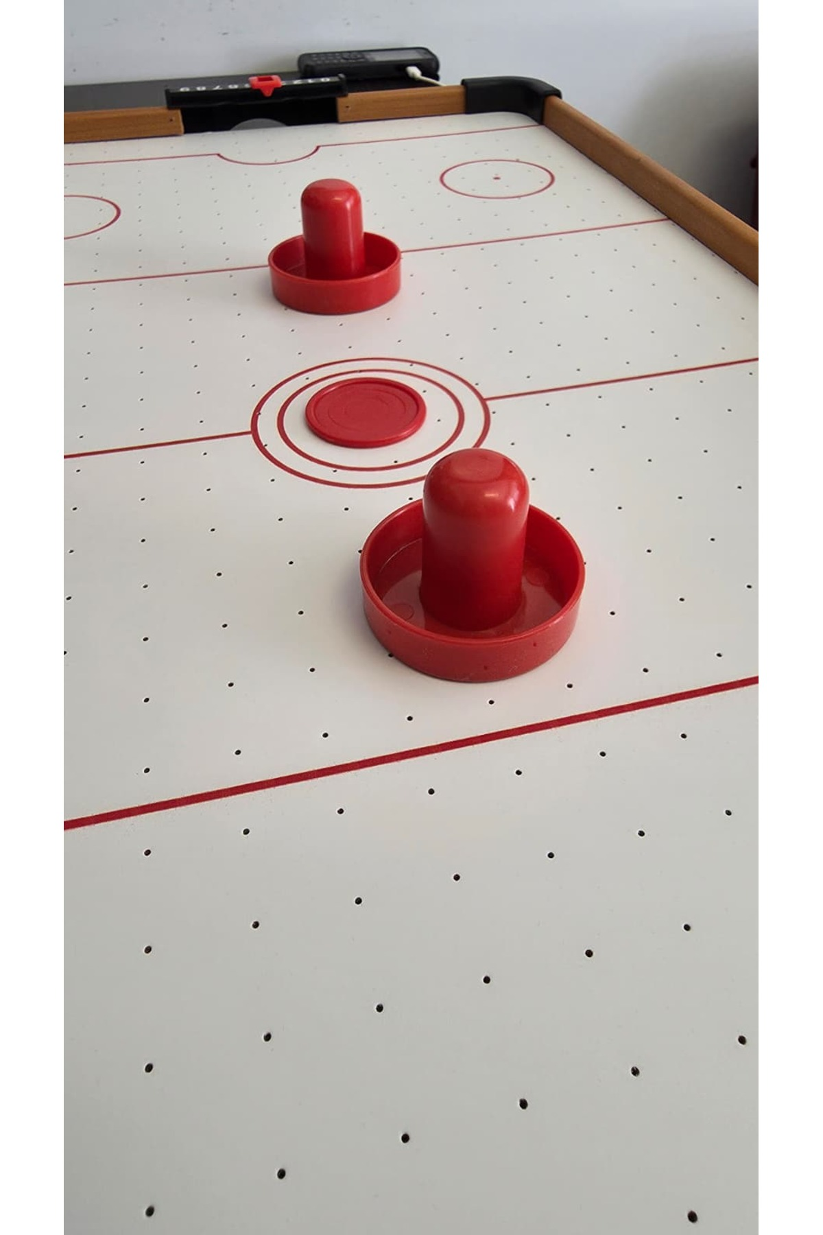 Ortasında iki k ırmızı tokmak ve bir kırmızı disk bulunan bir air hockey masası.