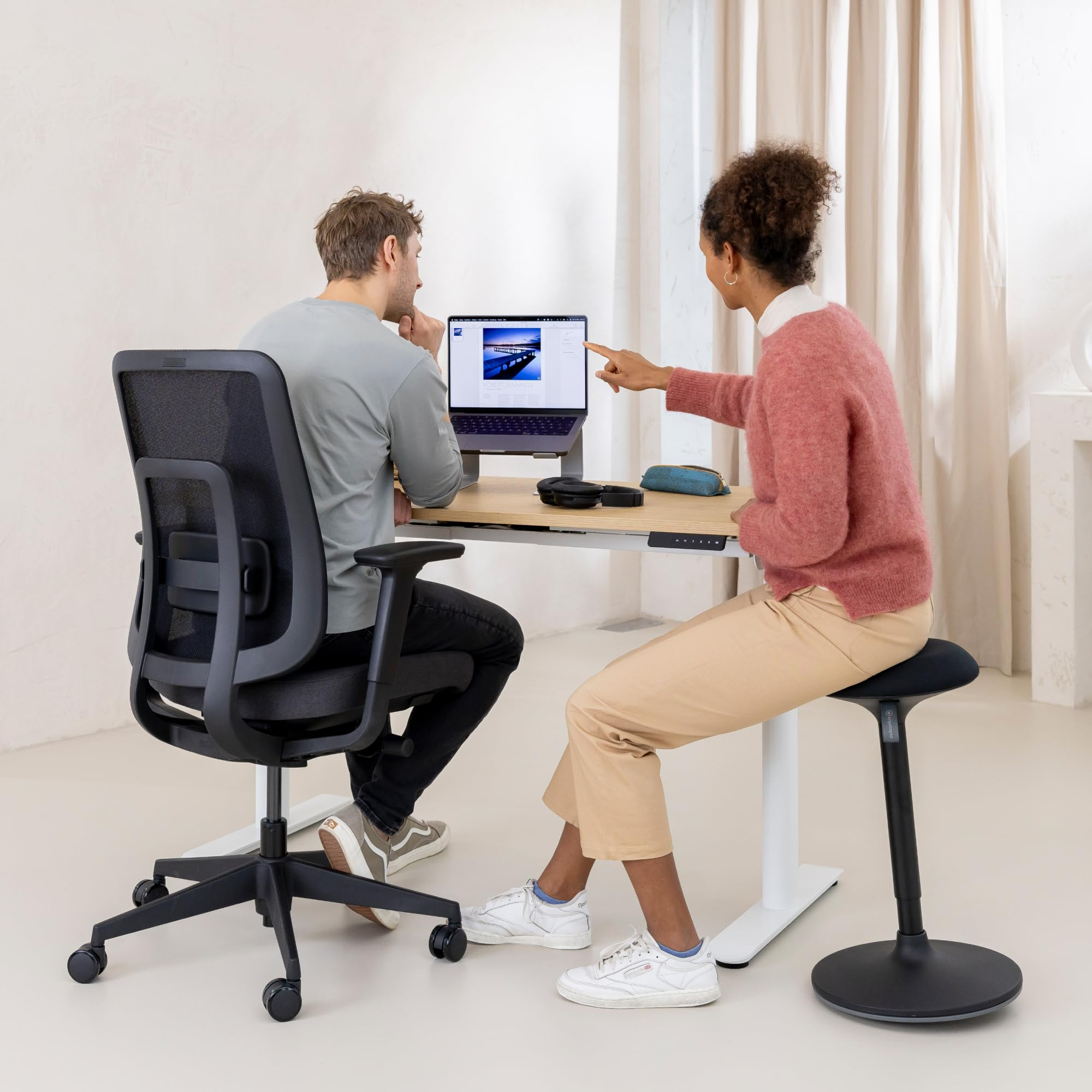 Deux collègues travaillent à un bureau debout, la femme pointant l'écran de l'ordinateur portable.