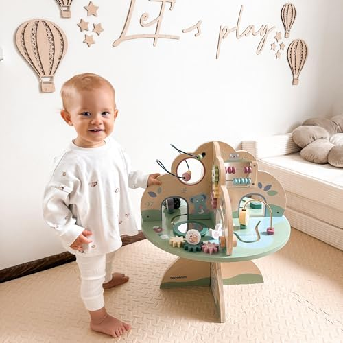 Un bambino piccolo con abiti bianchi accanto a un colorato tavolo di attività in legno.