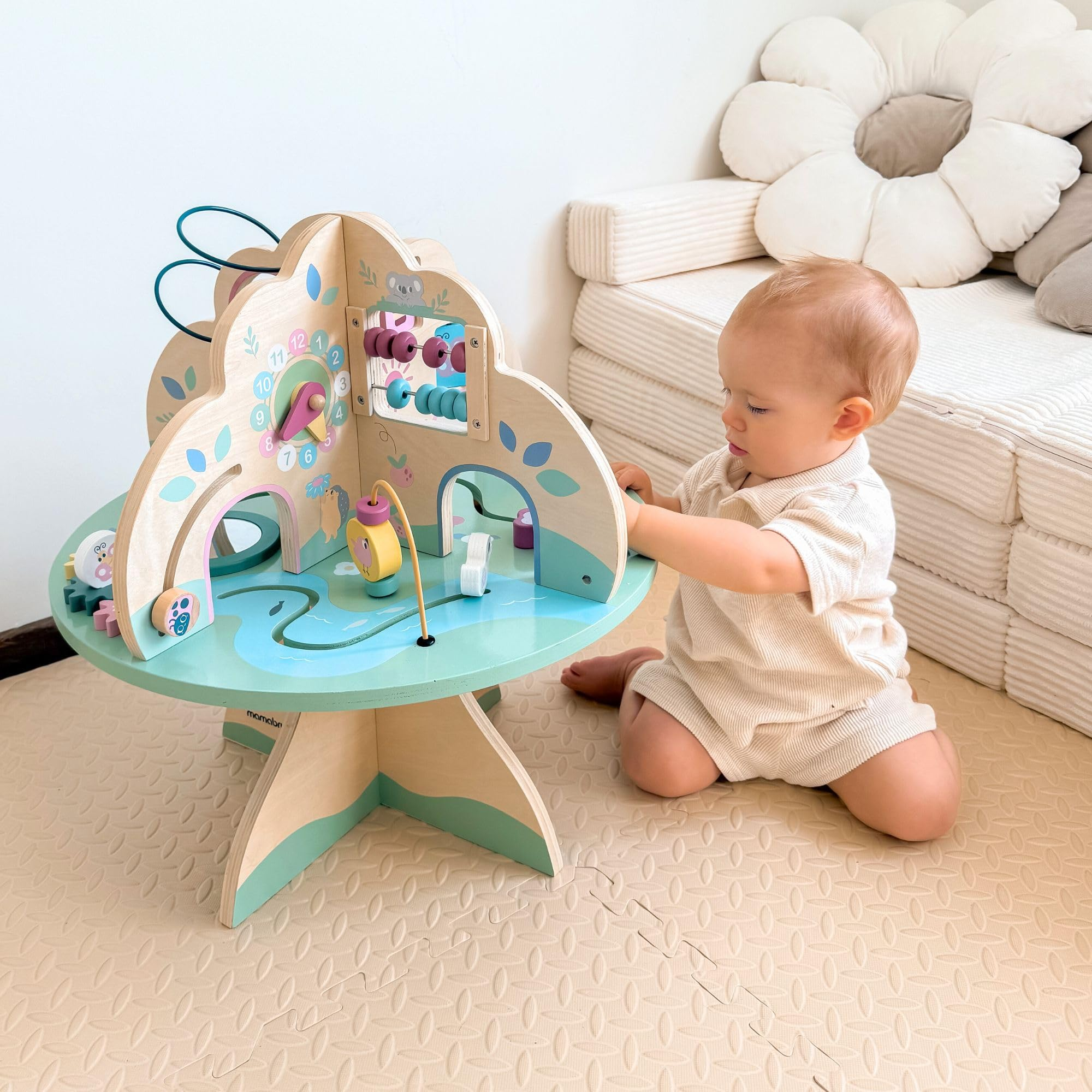 Bambino seduto sul pavimento che gioca con un colorato tavolo di attività in legno.