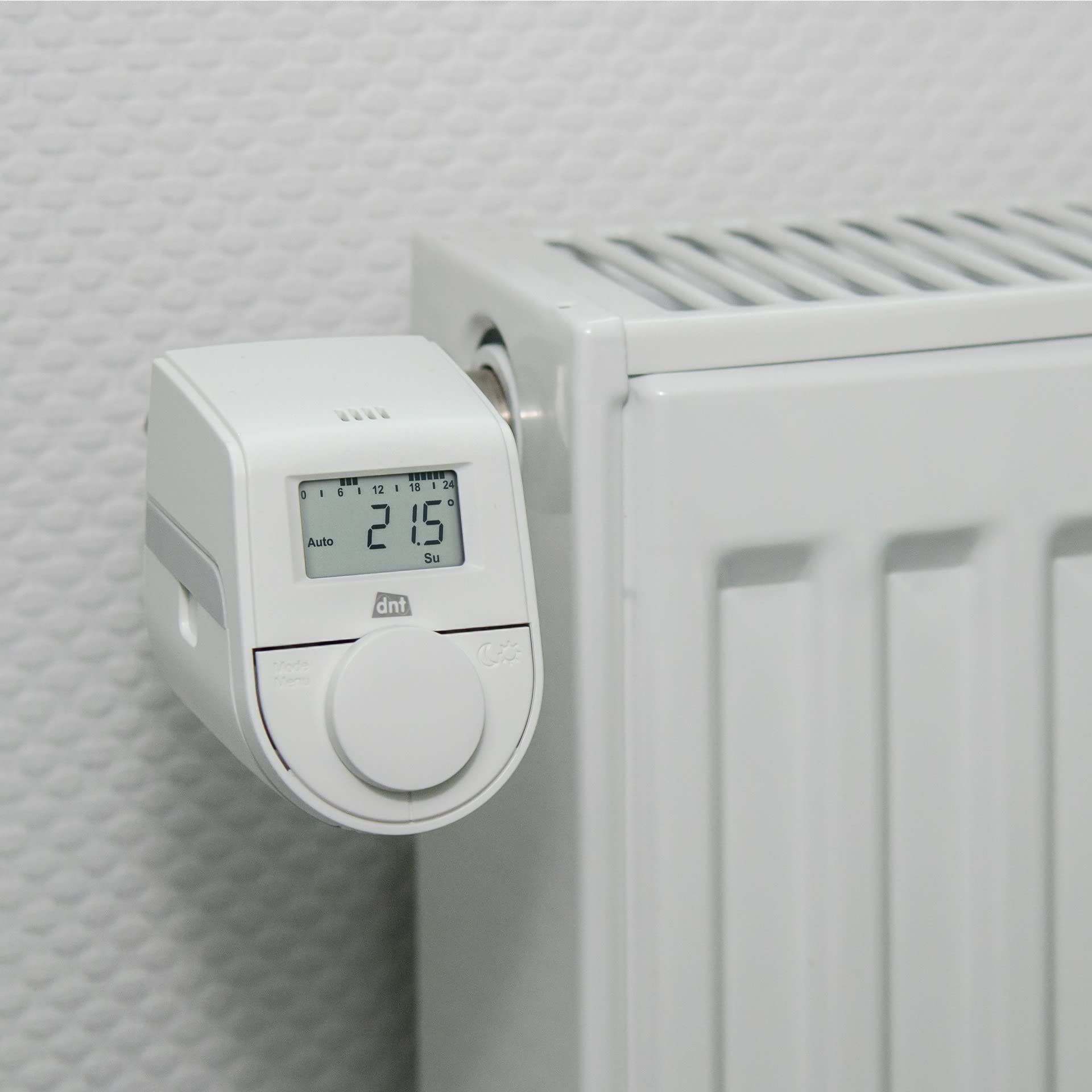 Ein weißes digitales Thermostat ist an einem weißen Heizkörper montiert und zeigt 21,5 Grad an.