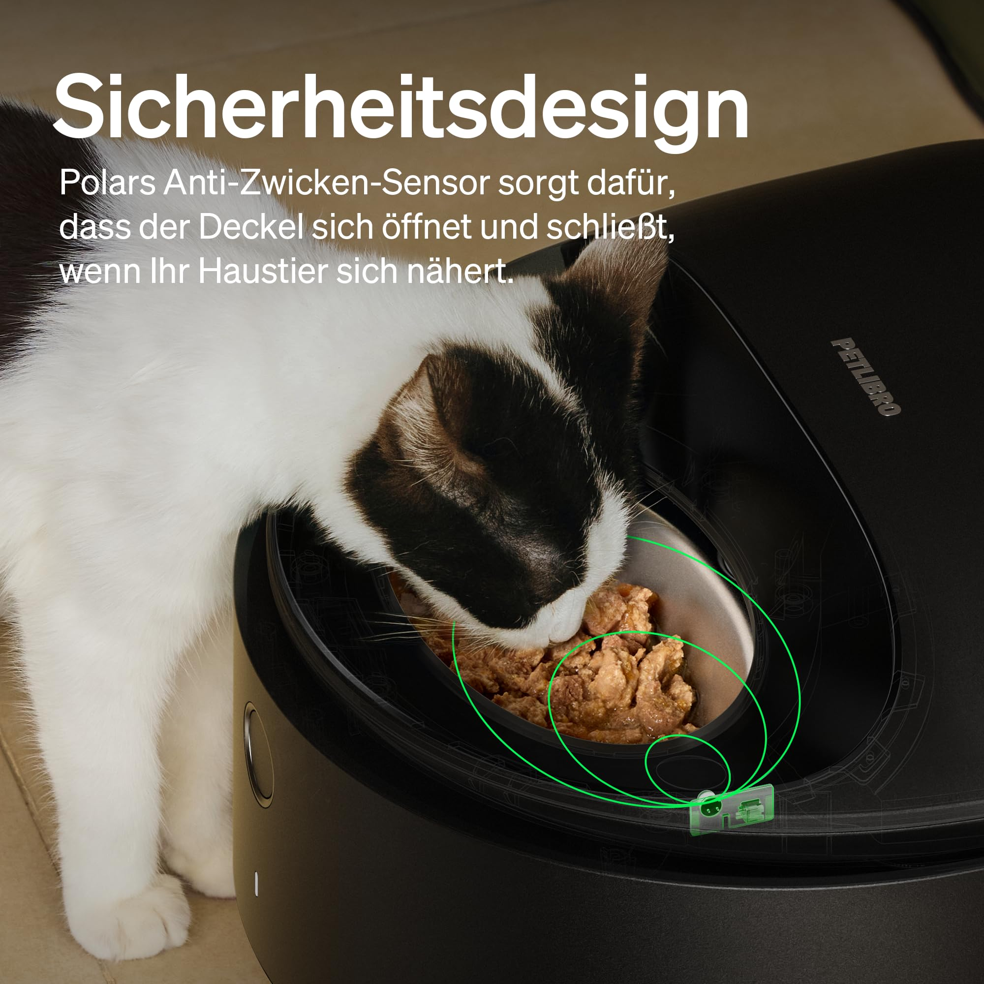 Un gatto bianco e nero mangia da una mangiatoia automatica nera.