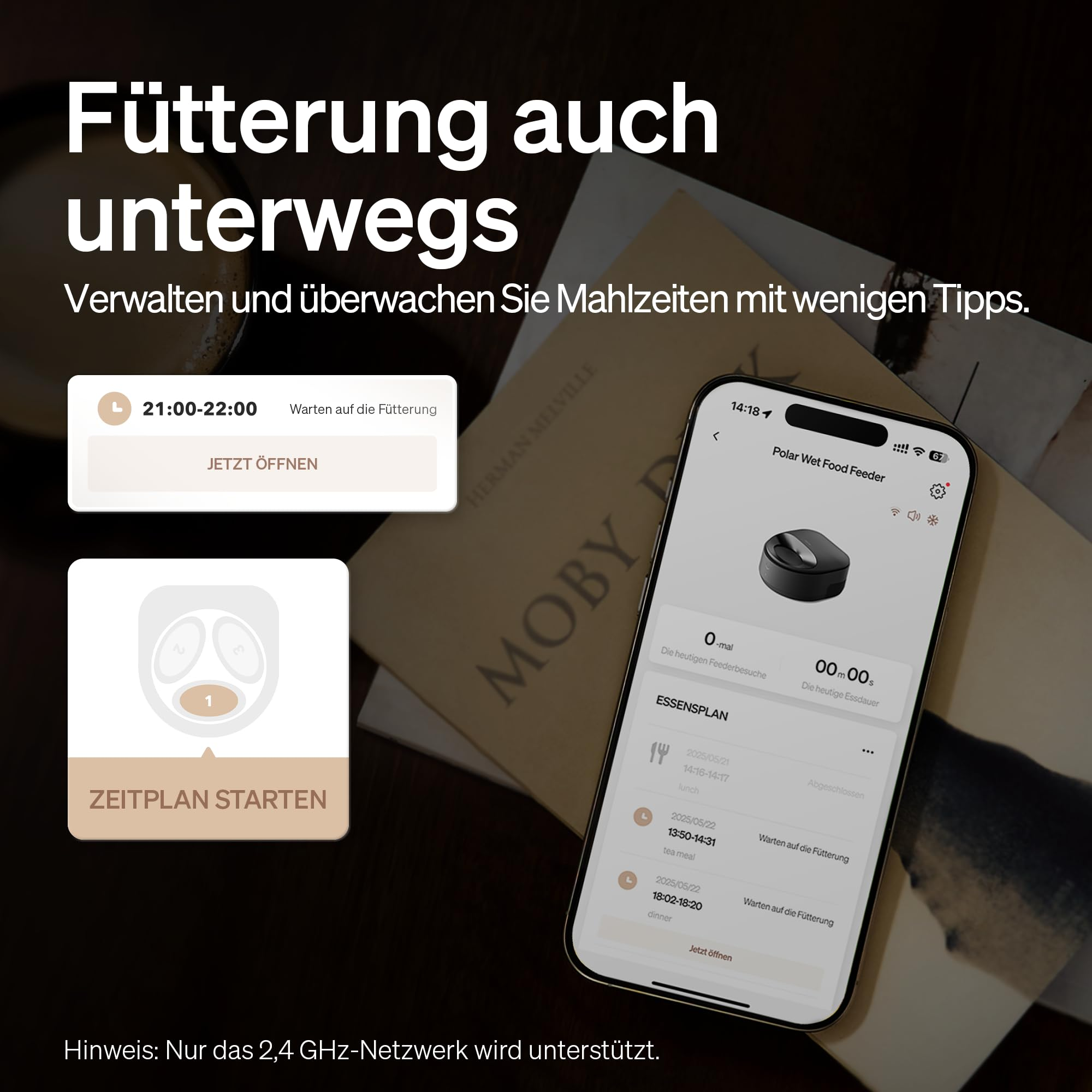 Smartphone con app per mangiatoia accanto a un libro e tazza, con testo in tedesco.