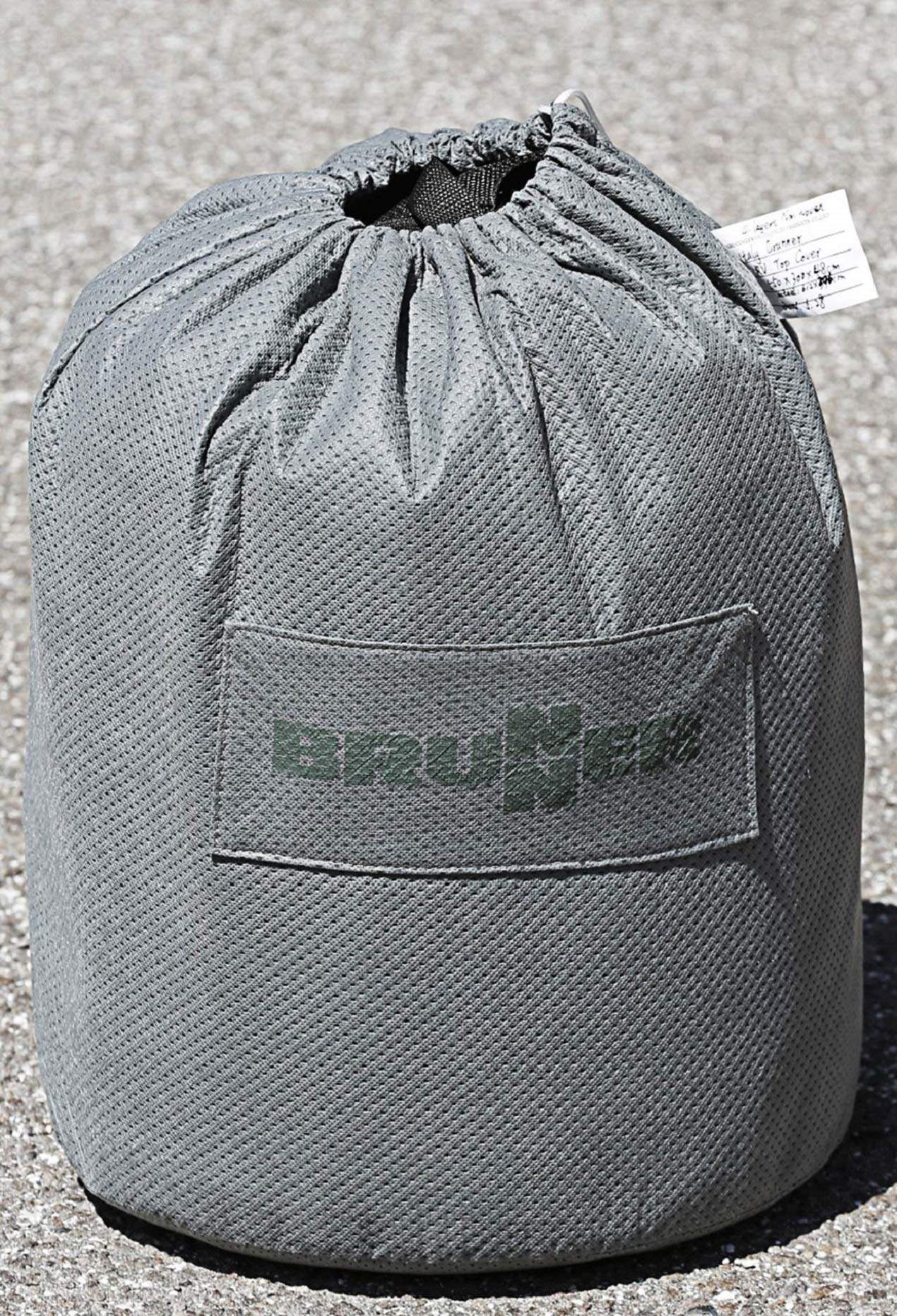 Grauer, runder Packsack aus Netzstoff mit Kordelzug und schwarzem Logo auf dem Boden auf Asphalt.