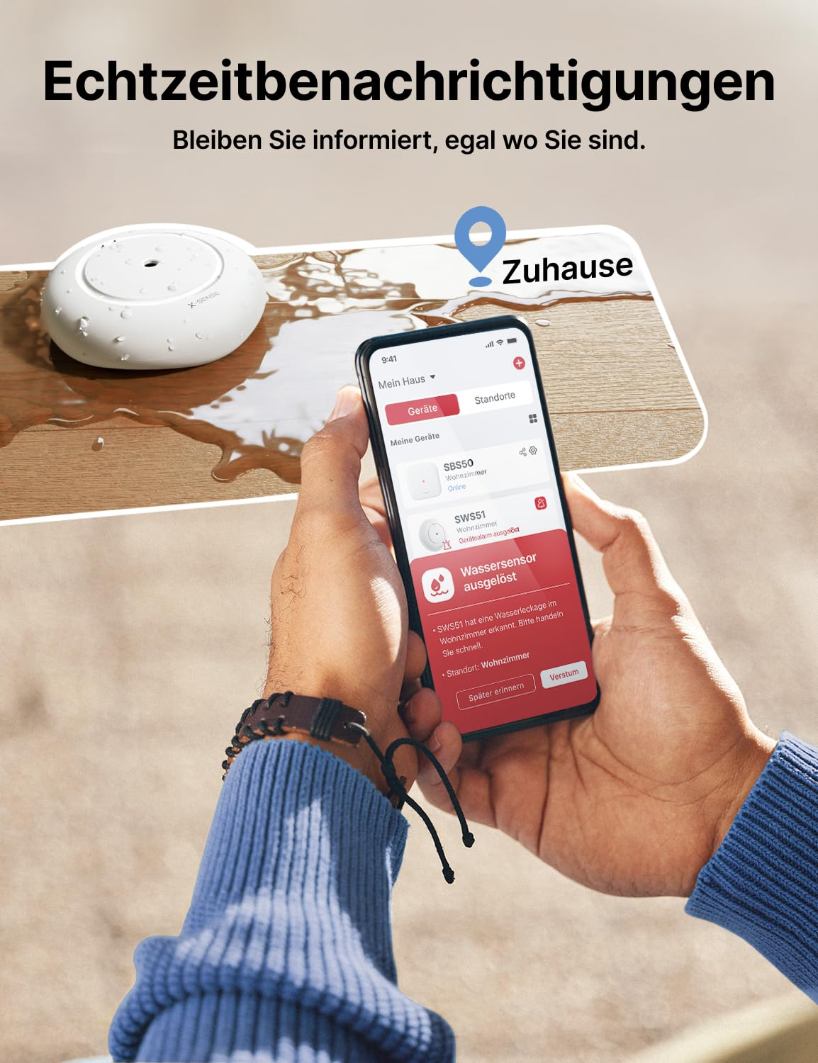 Smartphone in mano mostra l'avviso di perdita d'acqua di un'app, accanto a un sensore bagnato.