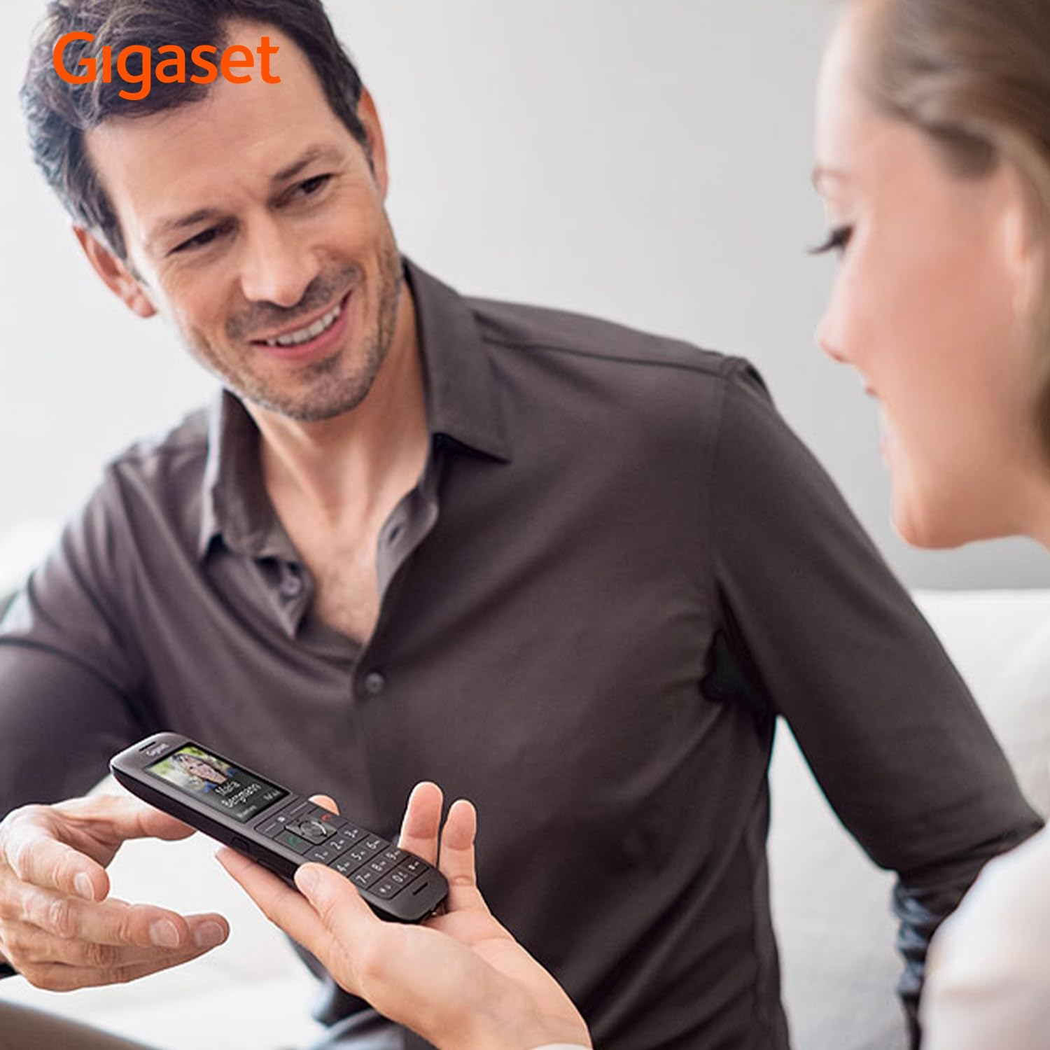 Un uomo sorridente in camicia grigia guarda una donna che tiene un telefono fisso Gigaset nero.