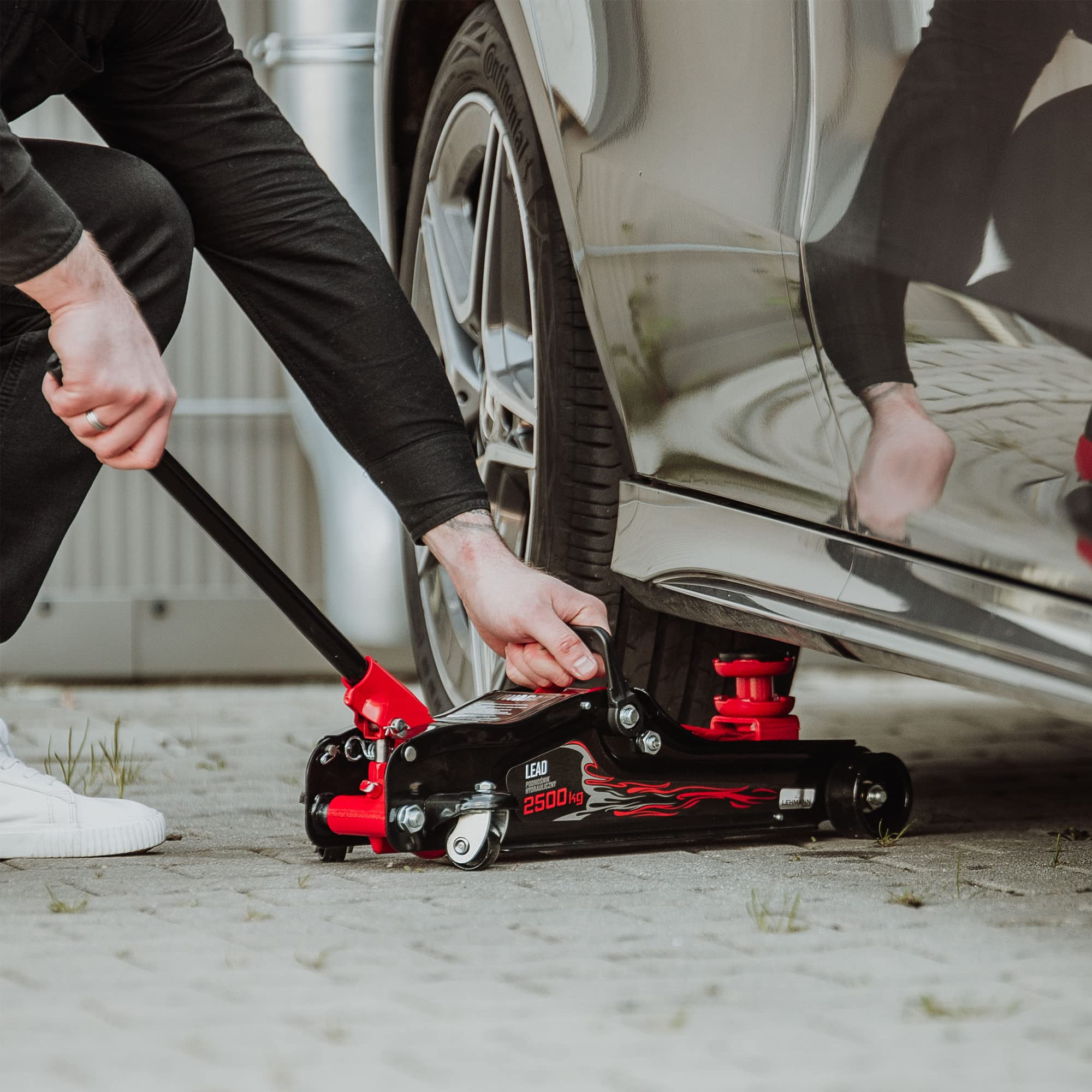 Una persona usa un cric idraulico nero e rosso per sollevare un'auto a terra.