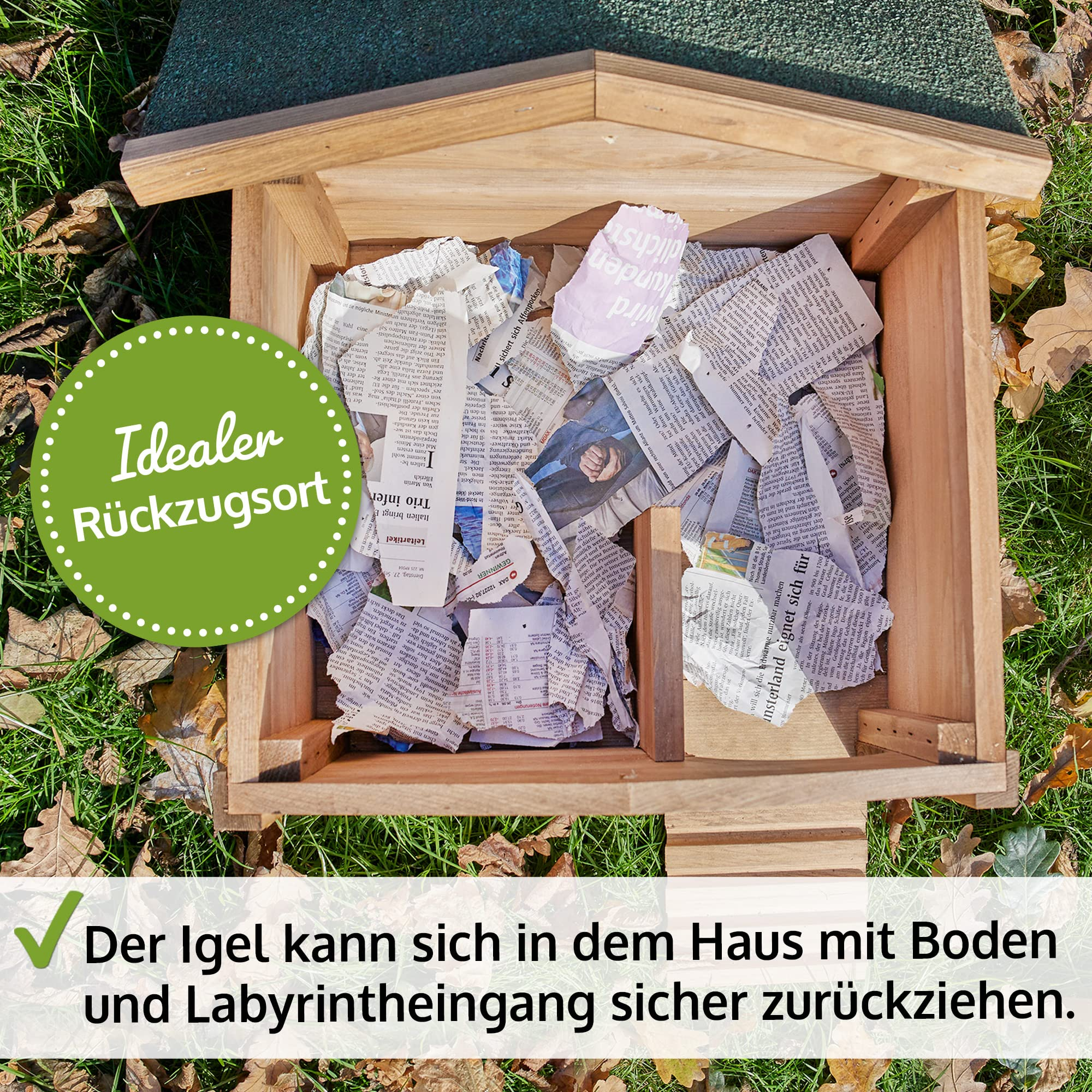 Une maison en bois pour hérissons vue du dessus remplie de journaux déchiquetés sur de l'herbe.