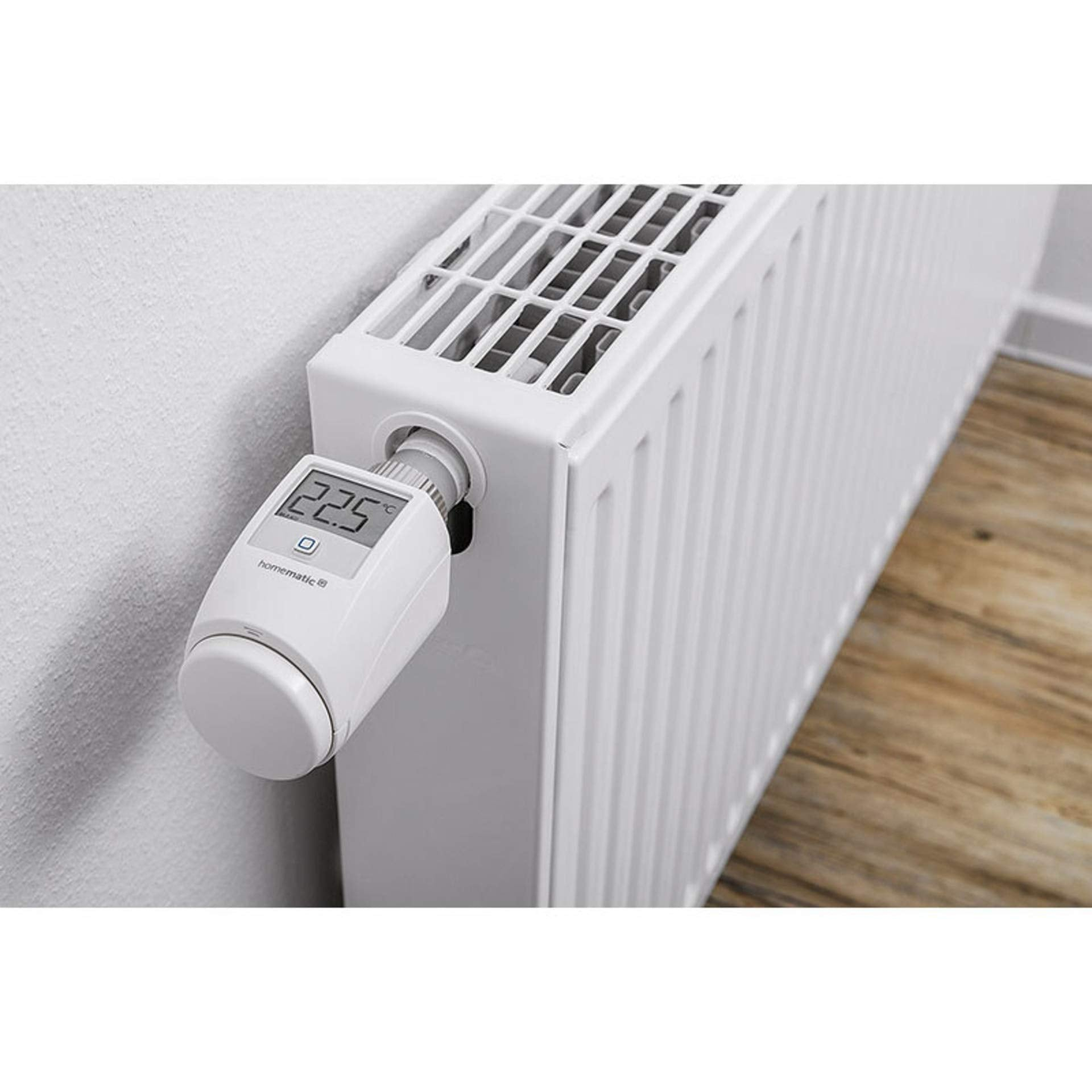Ein weißer Heizkörper mit digitalem Thermostatkopf, der 22,5 Grad Celsius anzeigt, in einem Raum mit Holzfußboden.
