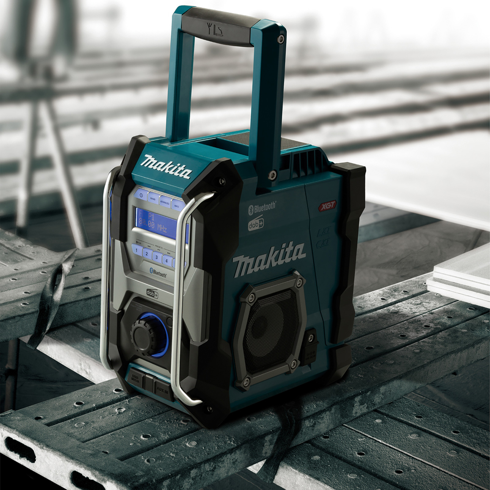 Una radio da cantiere Makita turchese e nera si trova su un'impalcatura metallica con sfondo sfocato.