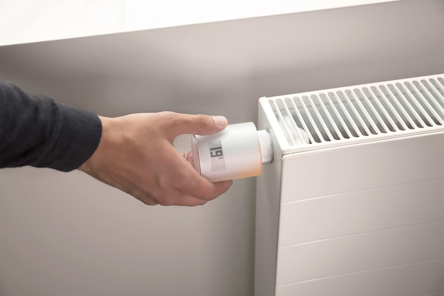 Eine Hand dreht das digitale Thermostat an einem weißen Heizkörper, um die Temperatur einzustellen.