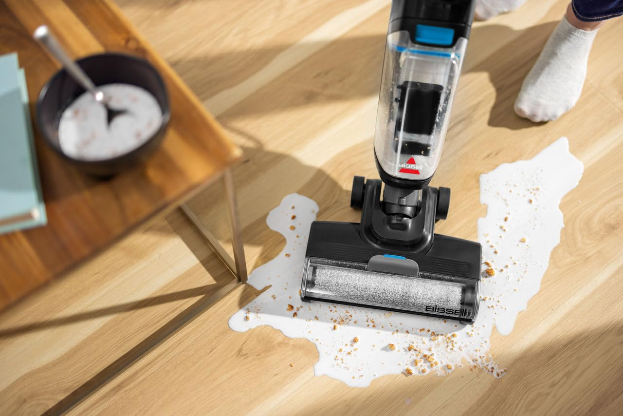 Un aspirapolvere senza fili per liquidi e solidi pulisce latte versato e briciole su un pavimento in legno.